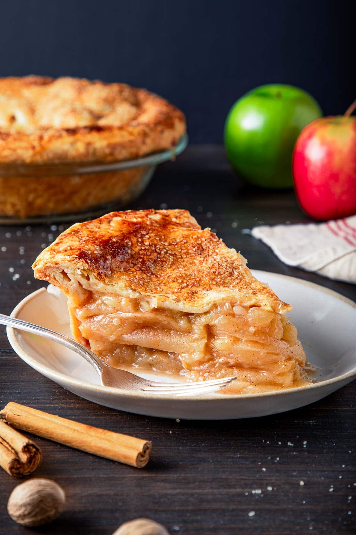 plate with a slice of apple pie with coarse sugar topping and a fork.
