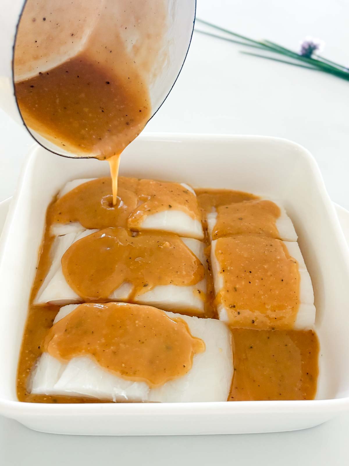 Pouring the miso marinade over the black cod filets in a baking dish. 