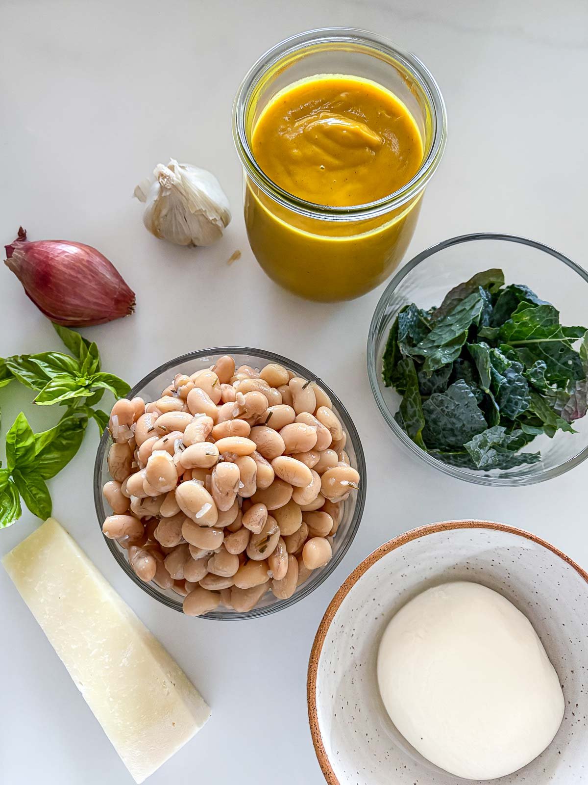 butternut baked beans with burrata ingredients - jar of butternut sauce, garlic, shallot, bowls of kale and white beans, basil, pecorino, and burrata.