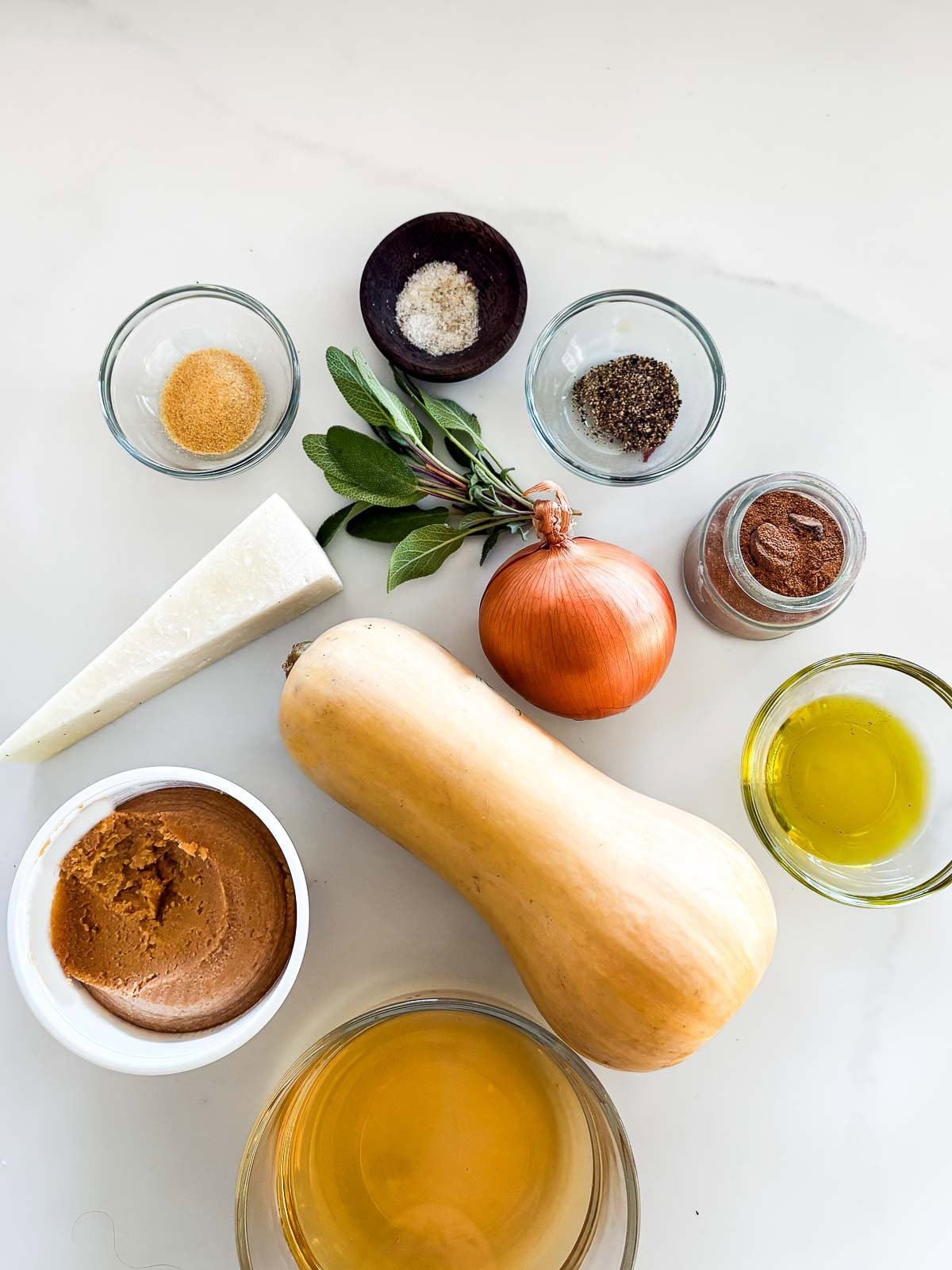 ingredients neatly arranged for butternut squash pasta sauce - granulated garlic, salt, pepper, nutmeg, olive oil, sage, onion, pecorino, butternut squash, miso paste, and broth.