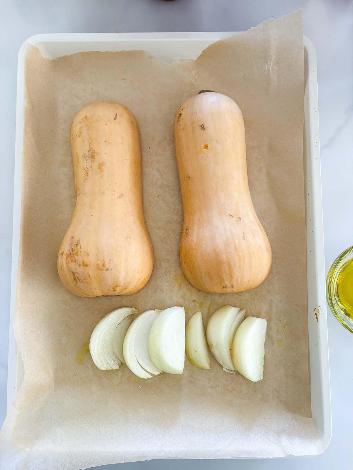 parchment-lined baking sheet with two butternut squash halves face down next to onion wedges.
