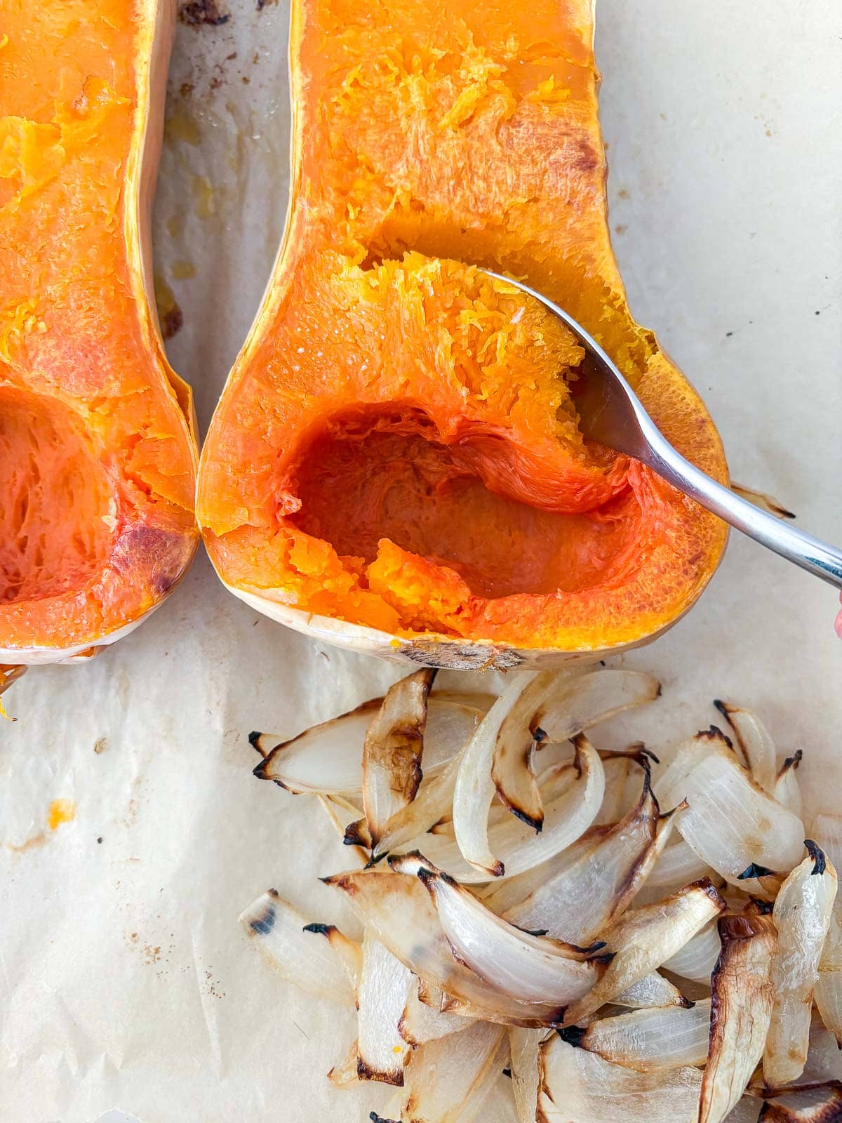 roasted butternut squash with spoon scooping out some of the caramelized flesh next to pile of roasted onions.