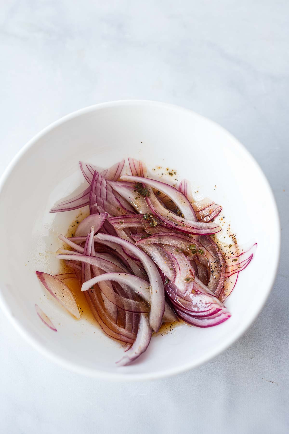 thinly sliced red onion in bowl in dressing.