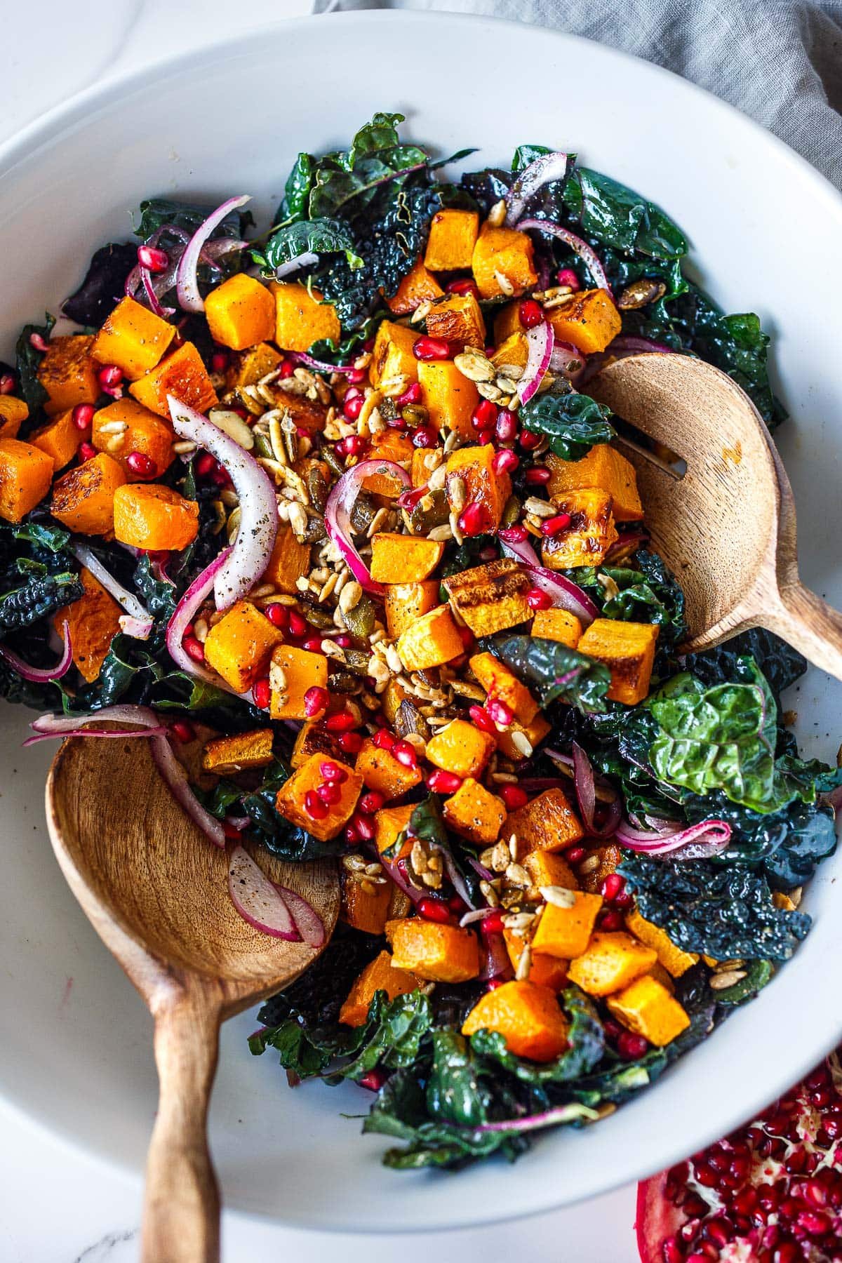 bowl of butternut squash kale salad topped with red onion, seeds, pomegranate seeds, and dried cranberries.