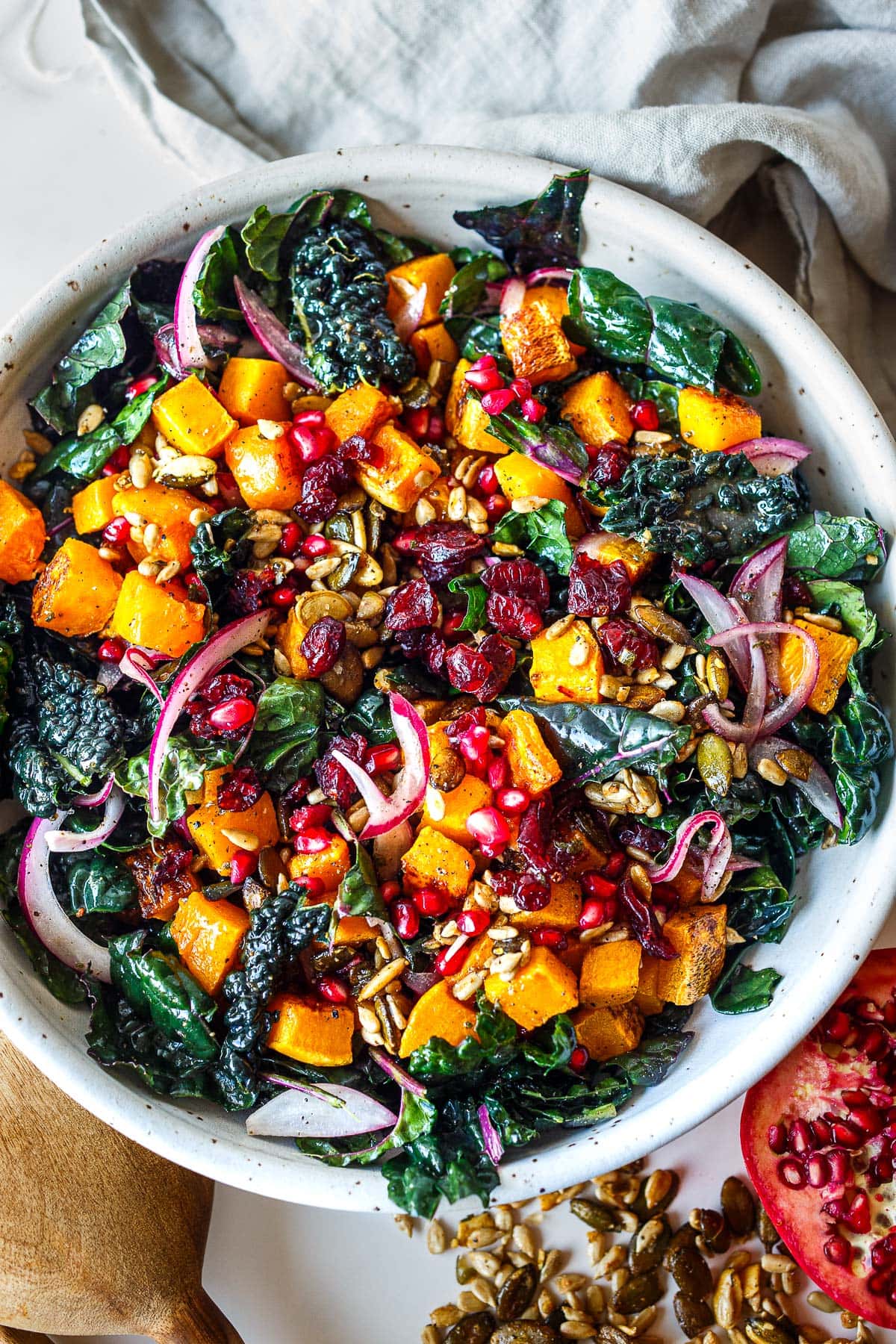 bowl of butternut squash kale salad topped with red onion, seeds, pomegranate seeds, and dried cranberries.