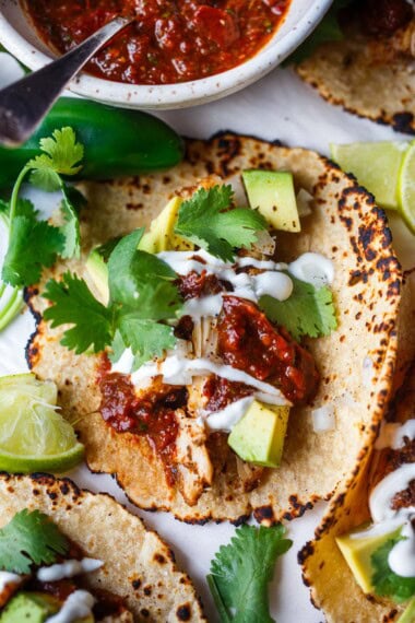 This chef-tested chicken taco recipe is easy and delicious! Made with tender, juicy baked chicken thighs, shredded and piled into warm tortillas with avocado, onions and cilantro- we serve it up street-taco style!
