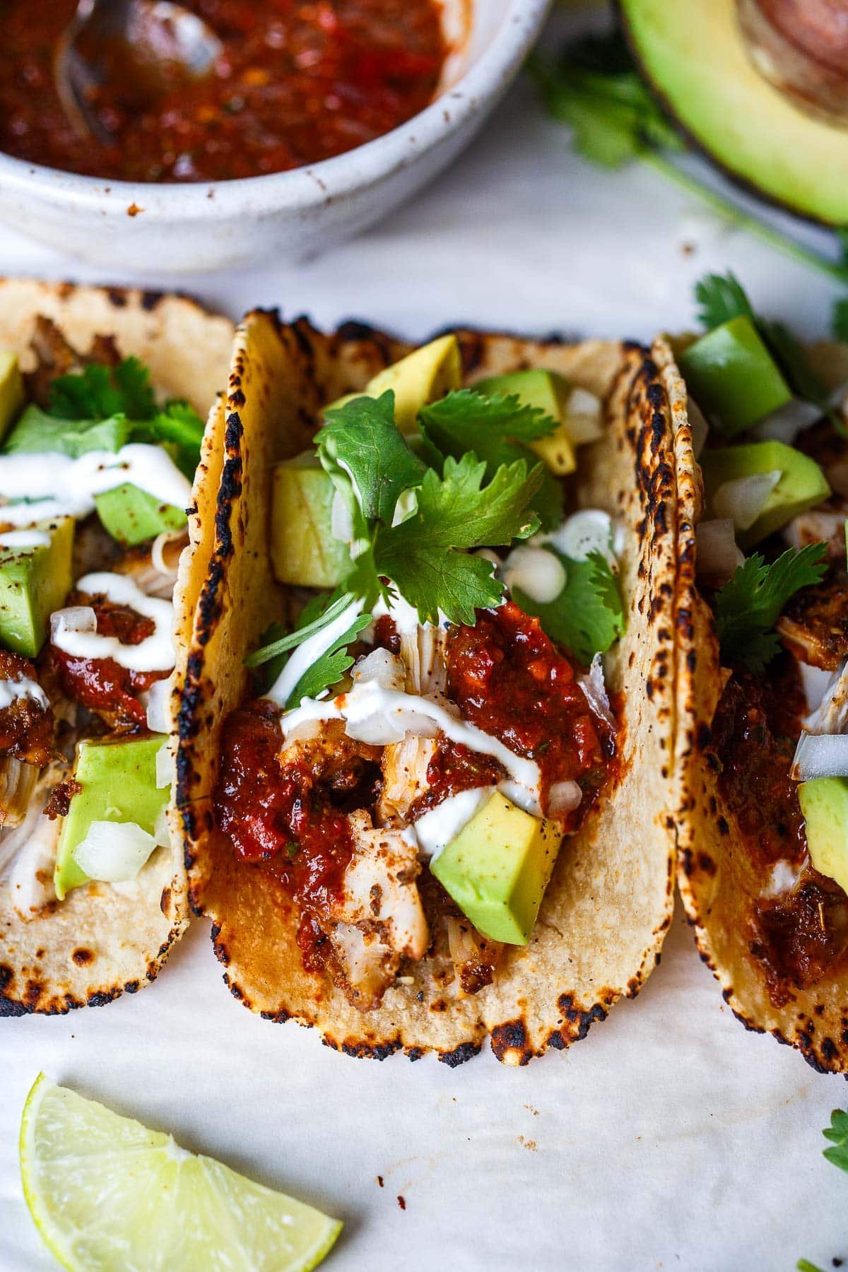 three chicken tacos topped with salsa roja, avocado, white onion, sour cream, cilantro.