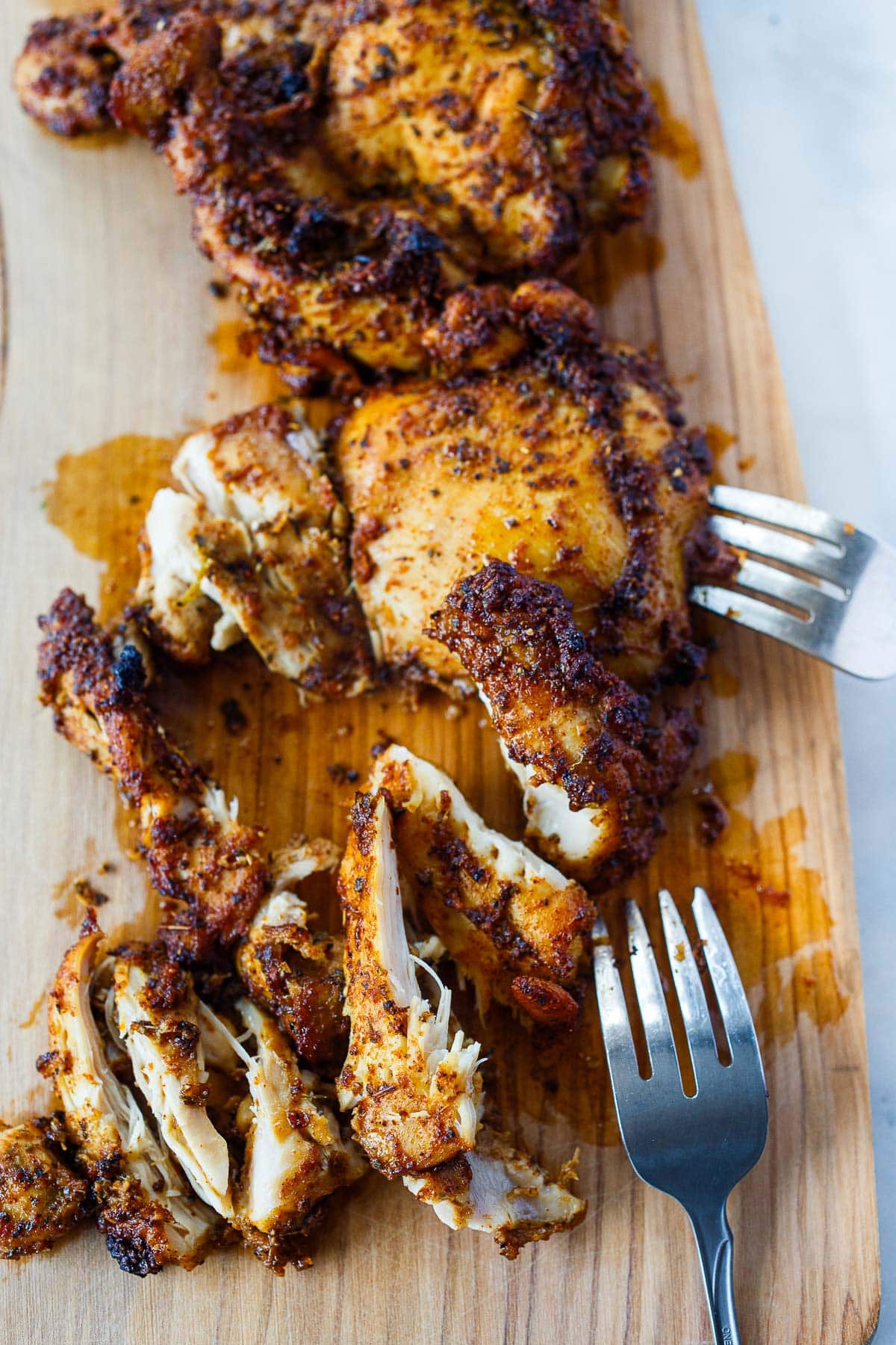forks shredding marinated baked chicken.