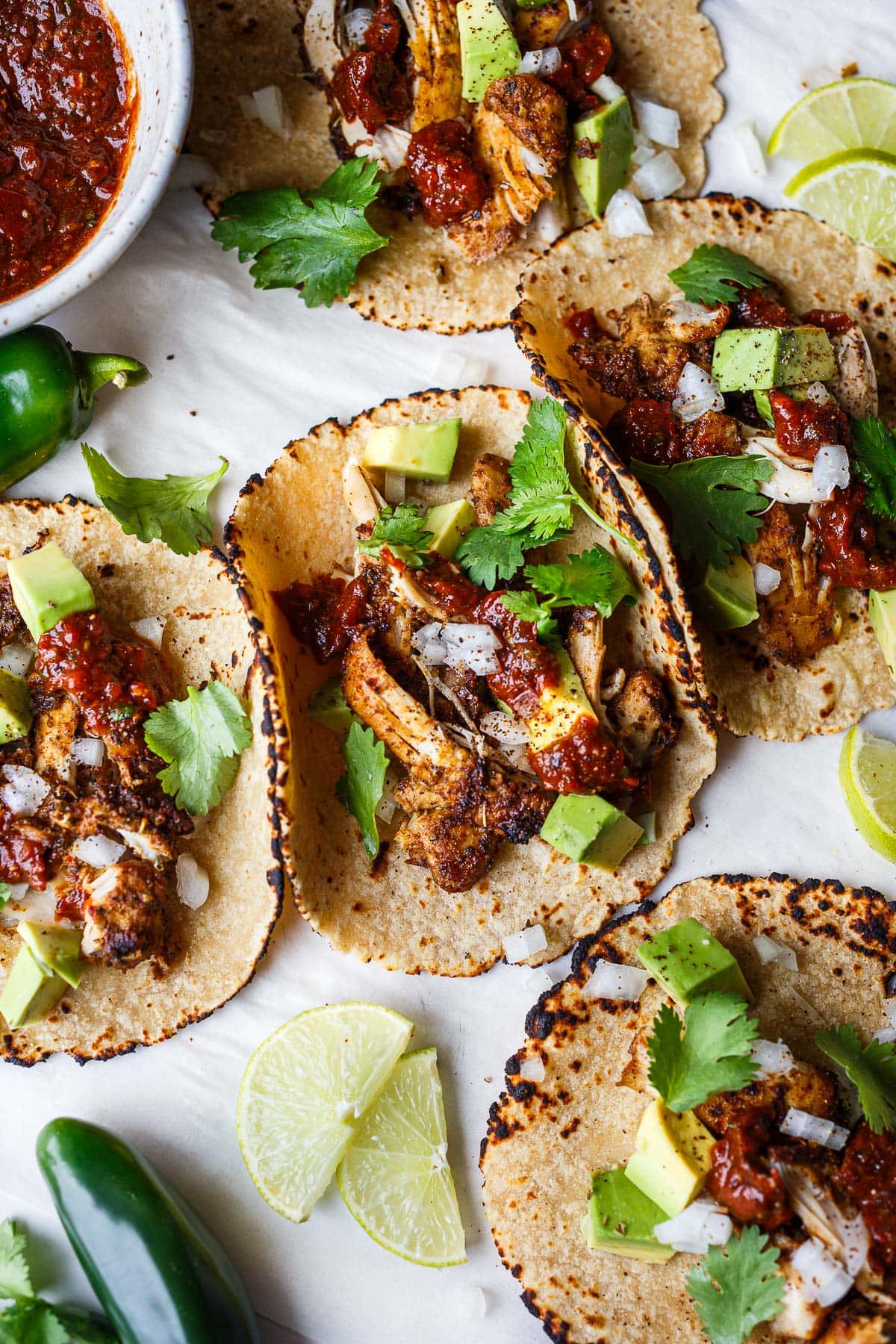 five chicken tacos topped with avocado, cilantro, white onion, and salsa roja.