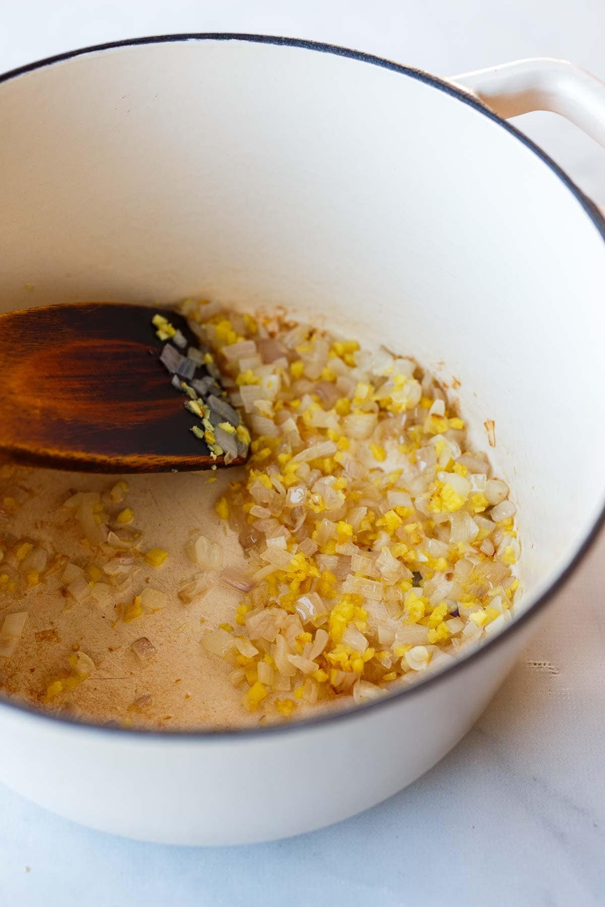 minced shallot, garlic, and ginger in a dutch oven with wood spatula.