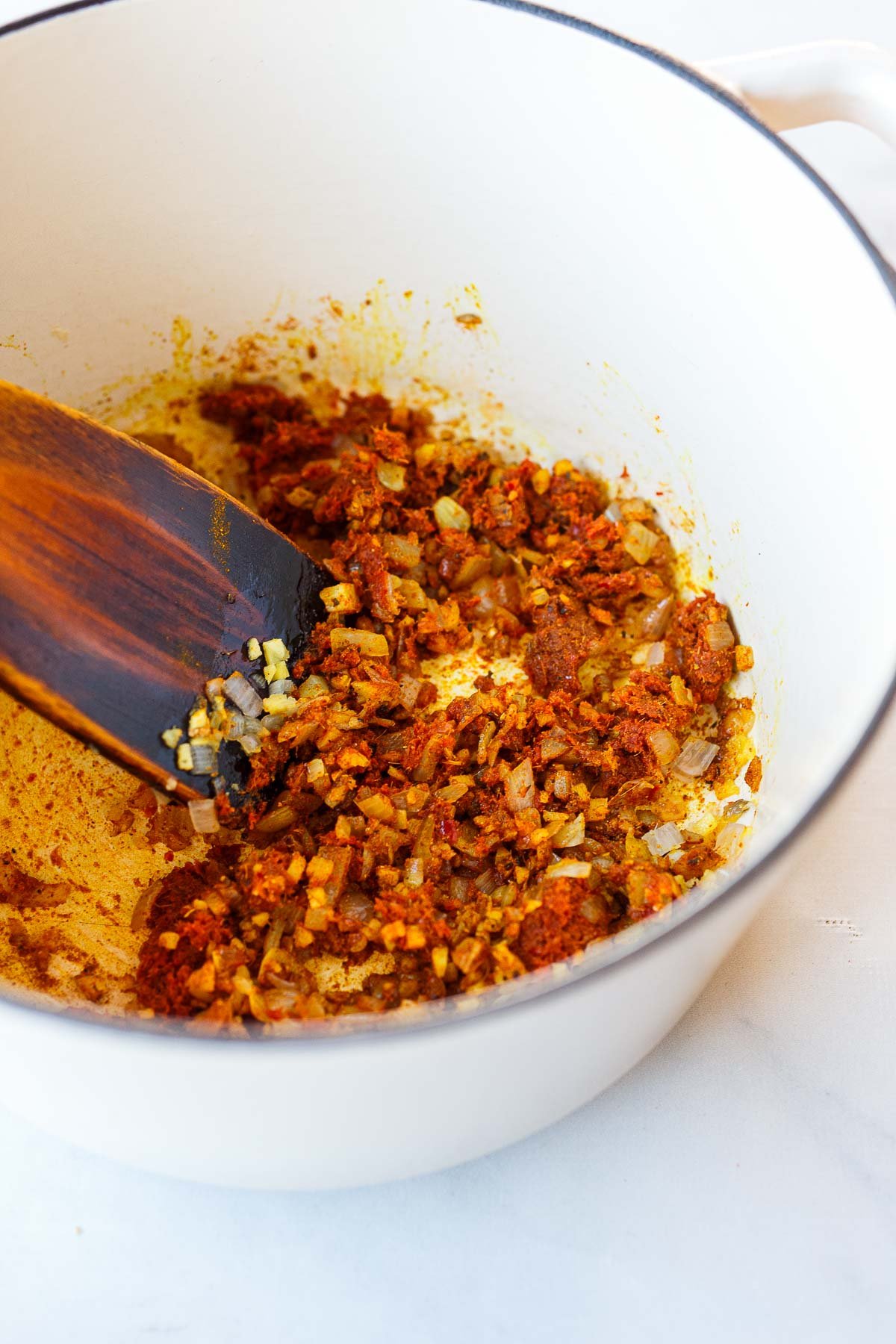 sautéed aromatics mixed with red curry paste and curry powder in dutch oven with wood spatula.