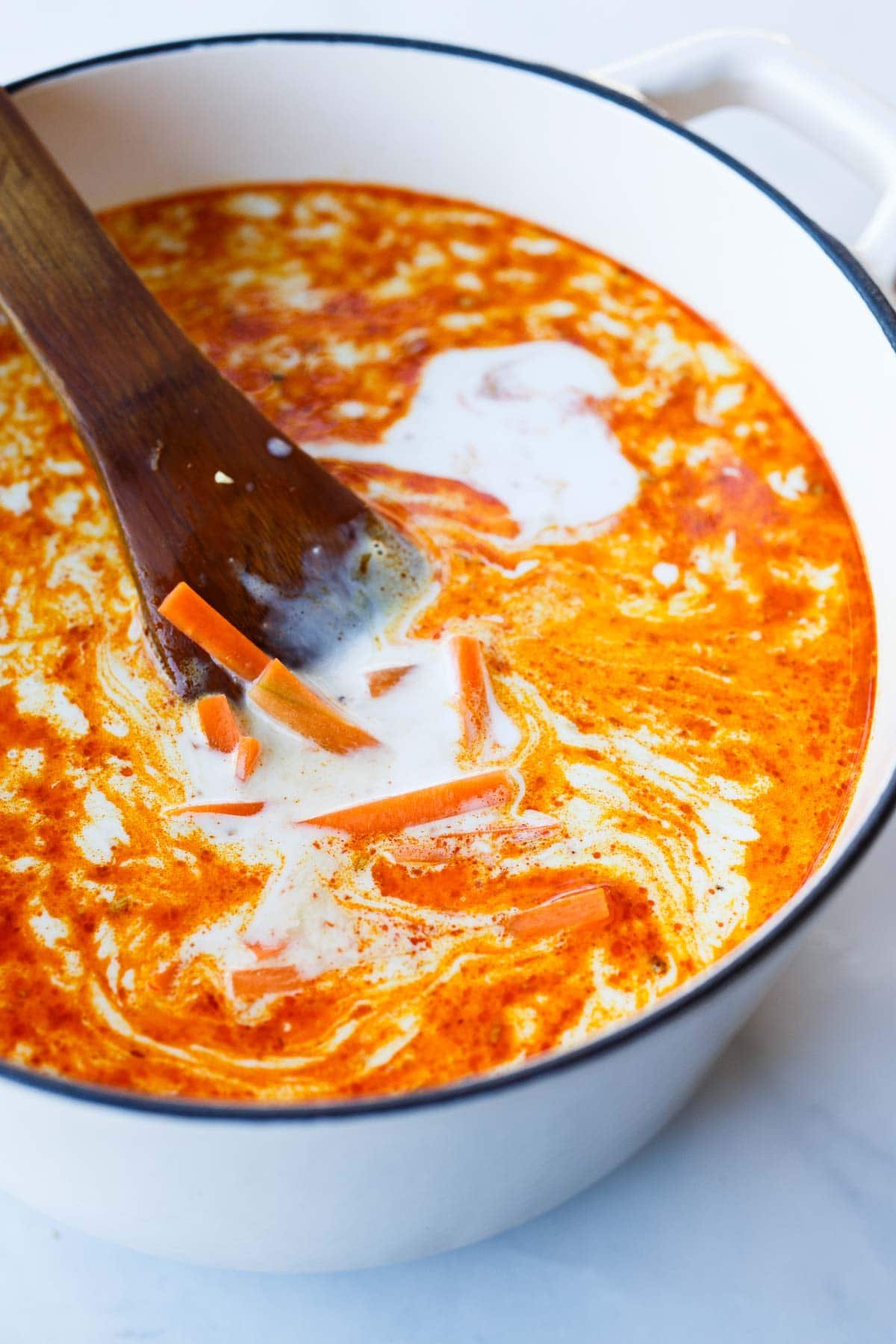 dutch oven with curry ramen broth infused with coconut milk and red curry paste with carrots.