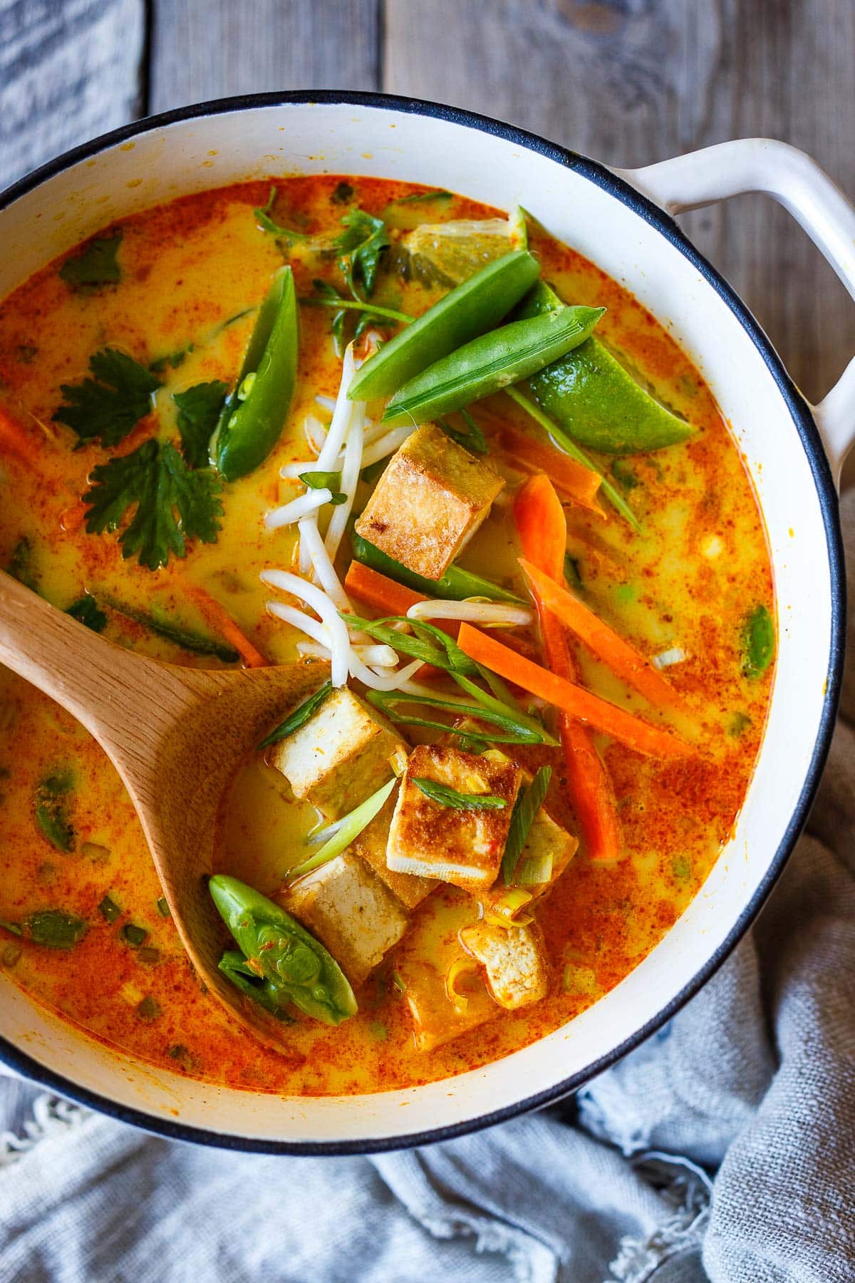dutch oven with curry ramen topped with crispy tofu cubes, carrots, snap peas, bean sprouts, cilantro, green onions, and lime wedges.