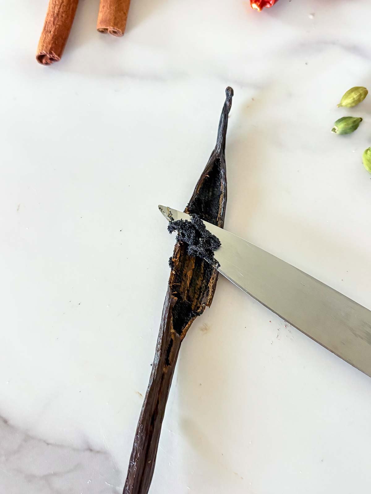 sharp knife scraping out the vanilla from the vanilla bean.