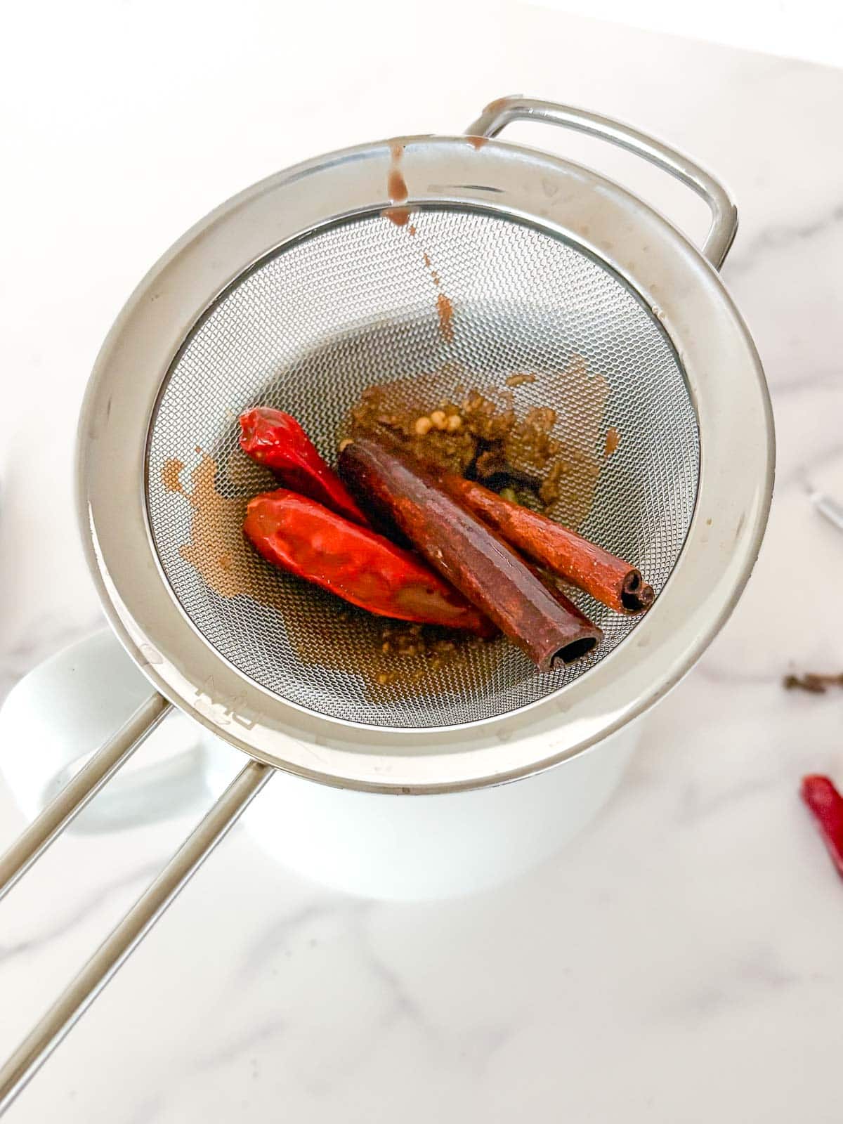 fine-mesh sieve with cinnamon sticks and dried red chilies, straining the Mexican hot chocolate.
