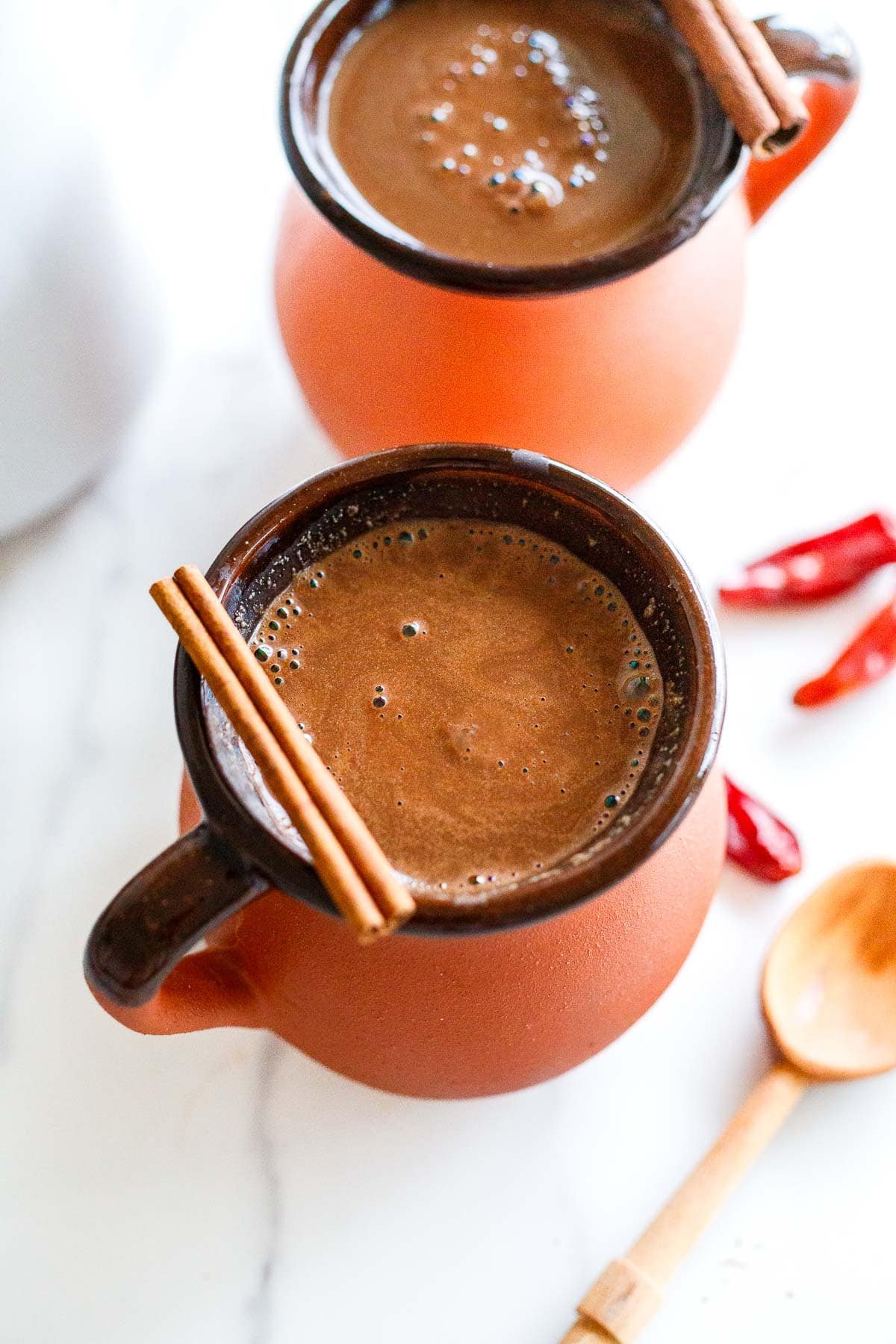 two ceramic mugs with Mexican hot chocolate with cinnamon sticks resting on top for garnish.
