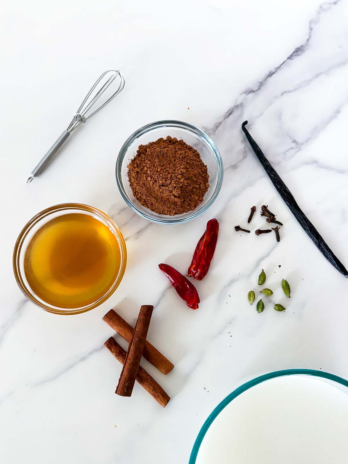 ingredients for Mexican hot chocolate - cacao, honey, cinnamon sticks, dried red chilies, whole cloves, cardamom pods, vanilla bean, and milk.