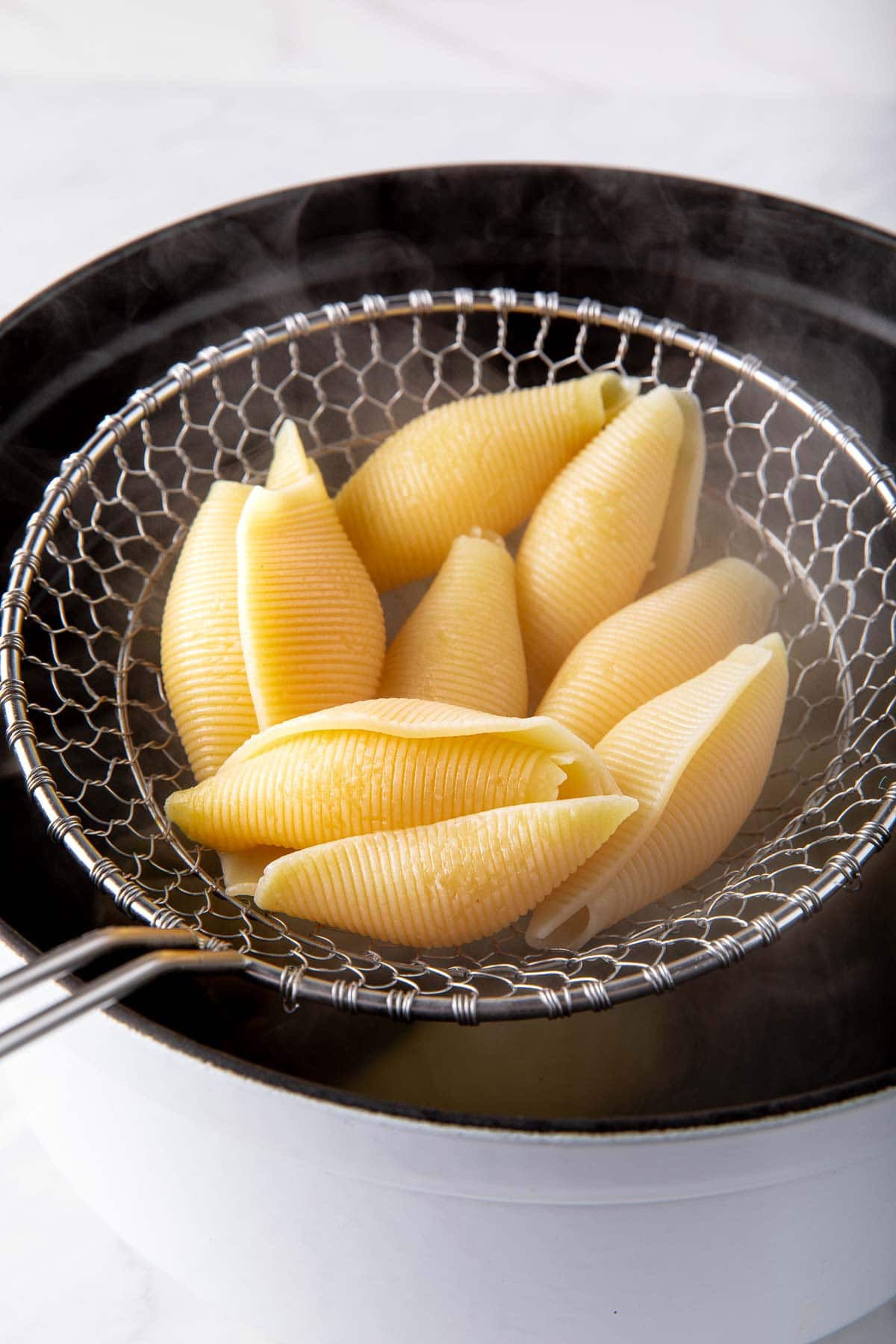 colander lifting jumbo shells out of the pot.