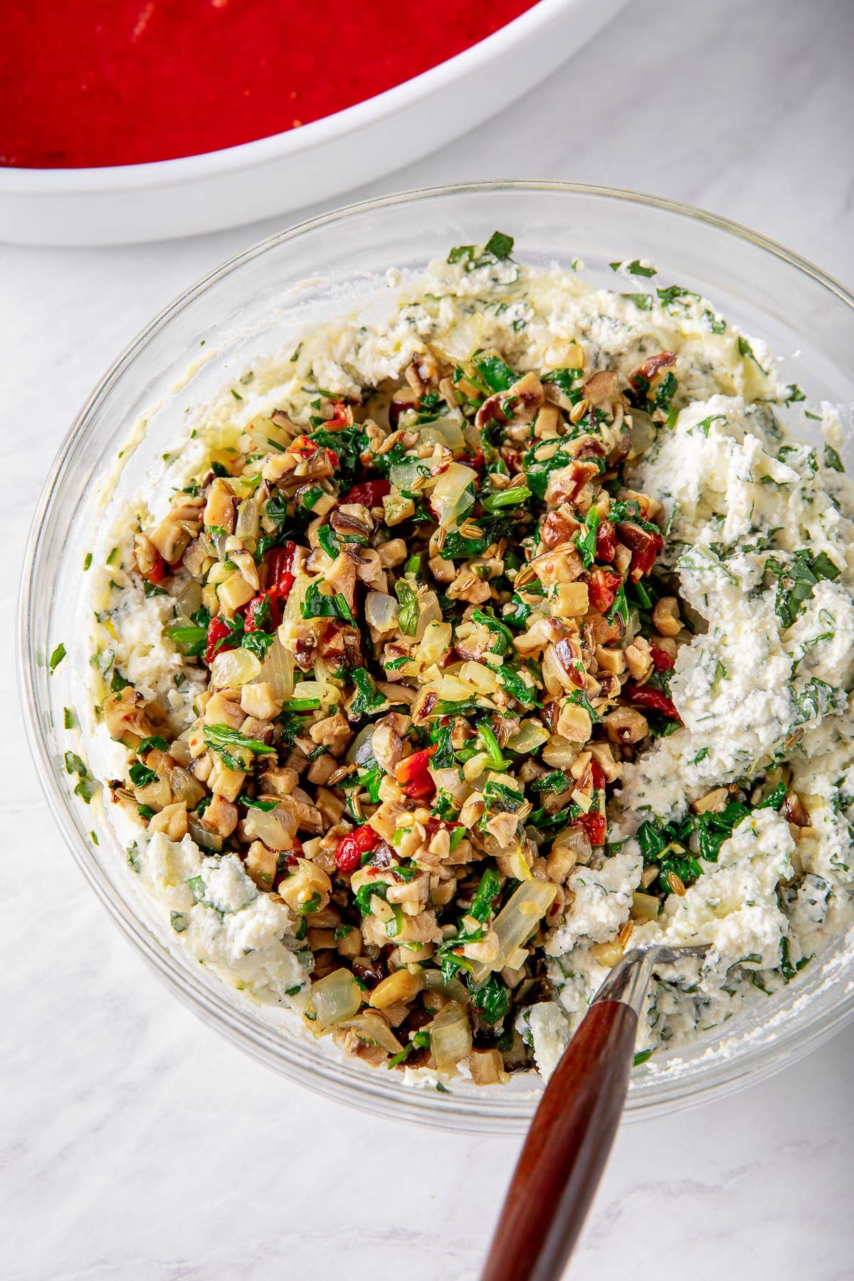 glass mixing bowl with sautéed veggies and ricotta mixture.