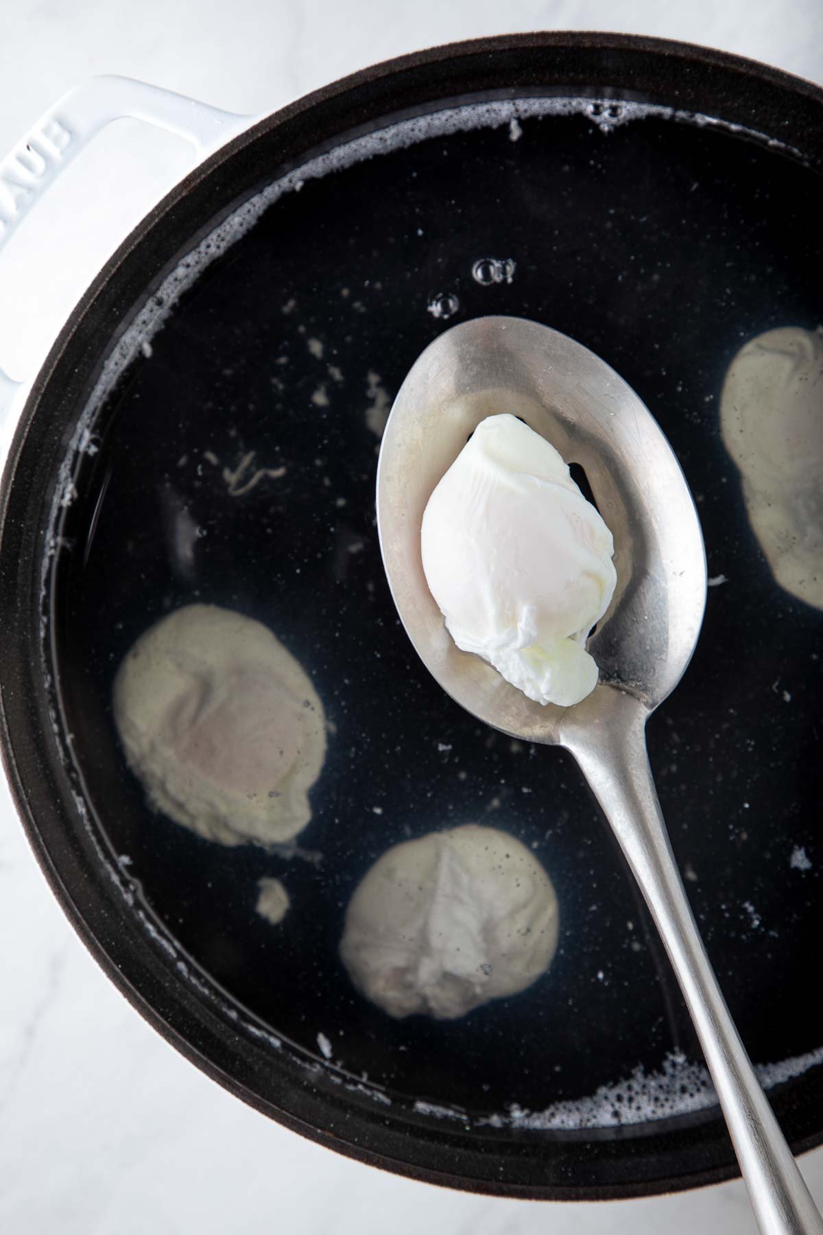 slotted spoon lifting poached egg out of pot of water. 