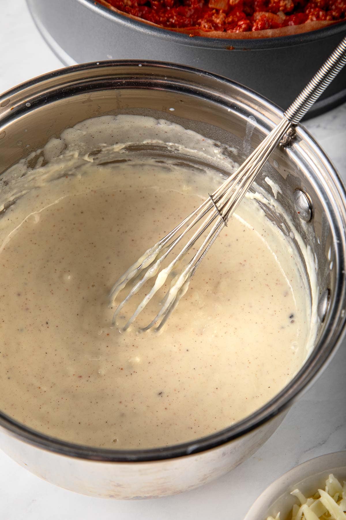 saucepan with béchamel sauce and whisk.
