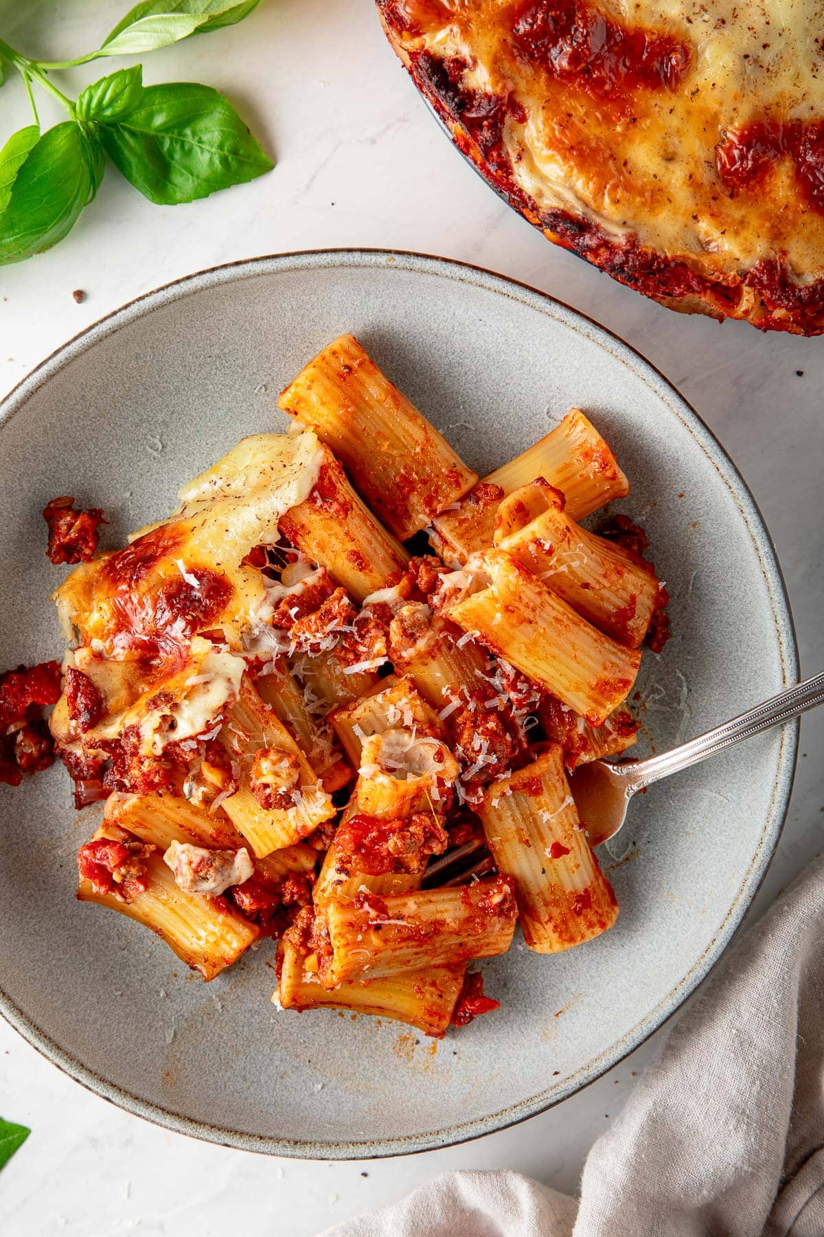 plate with serving of baked rigatoni with fork with some of the béchamel layer and topped with grated pecorino.