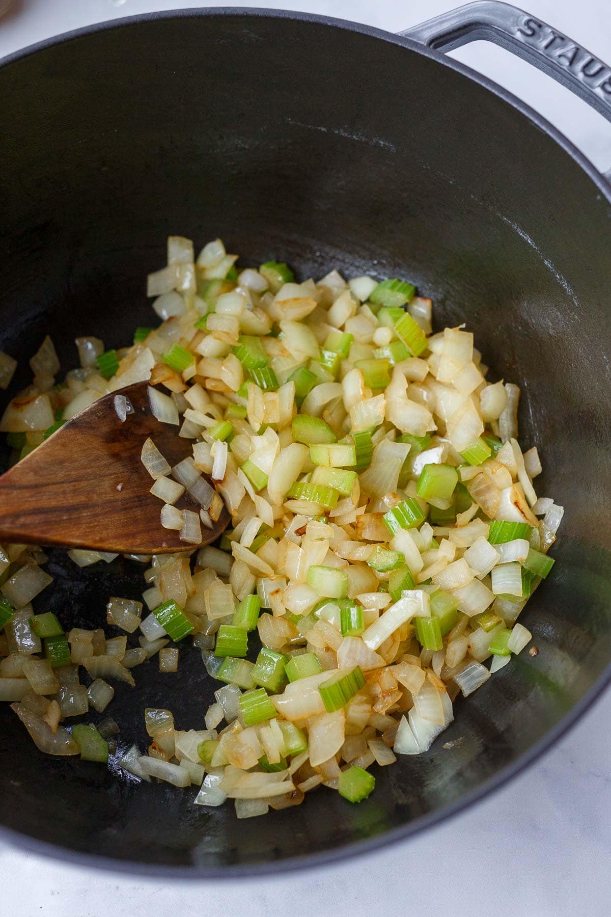 Dutch oven with onions and celery sautéing with wood spatula.