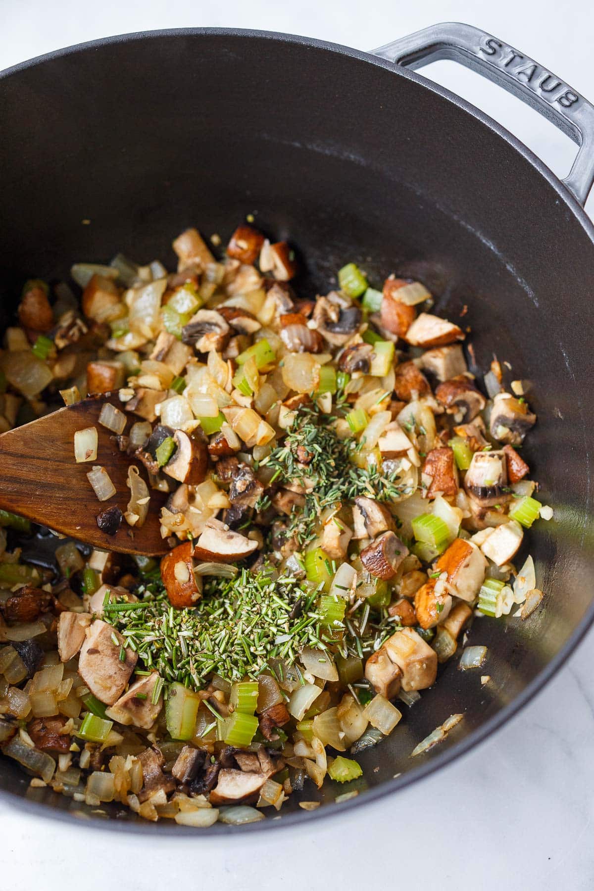 building the base for vegetable barley soup - onions, mushrooms, celery, and fresh, minced herbs in Dutch oven with wood spoon.