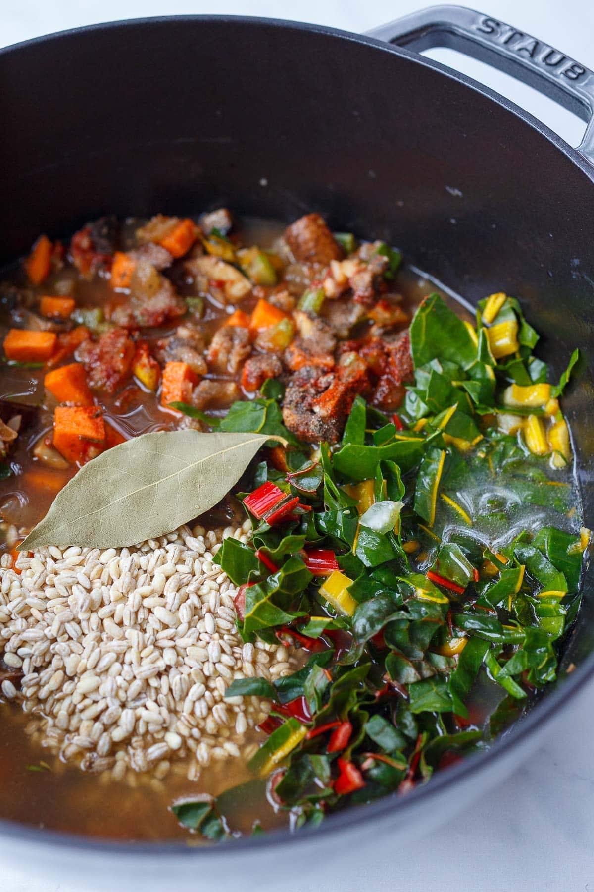 making vegetable barley soup - Dutch oven with veggies, chard, tomato paste, bay leaf, broth, and pearled barley.