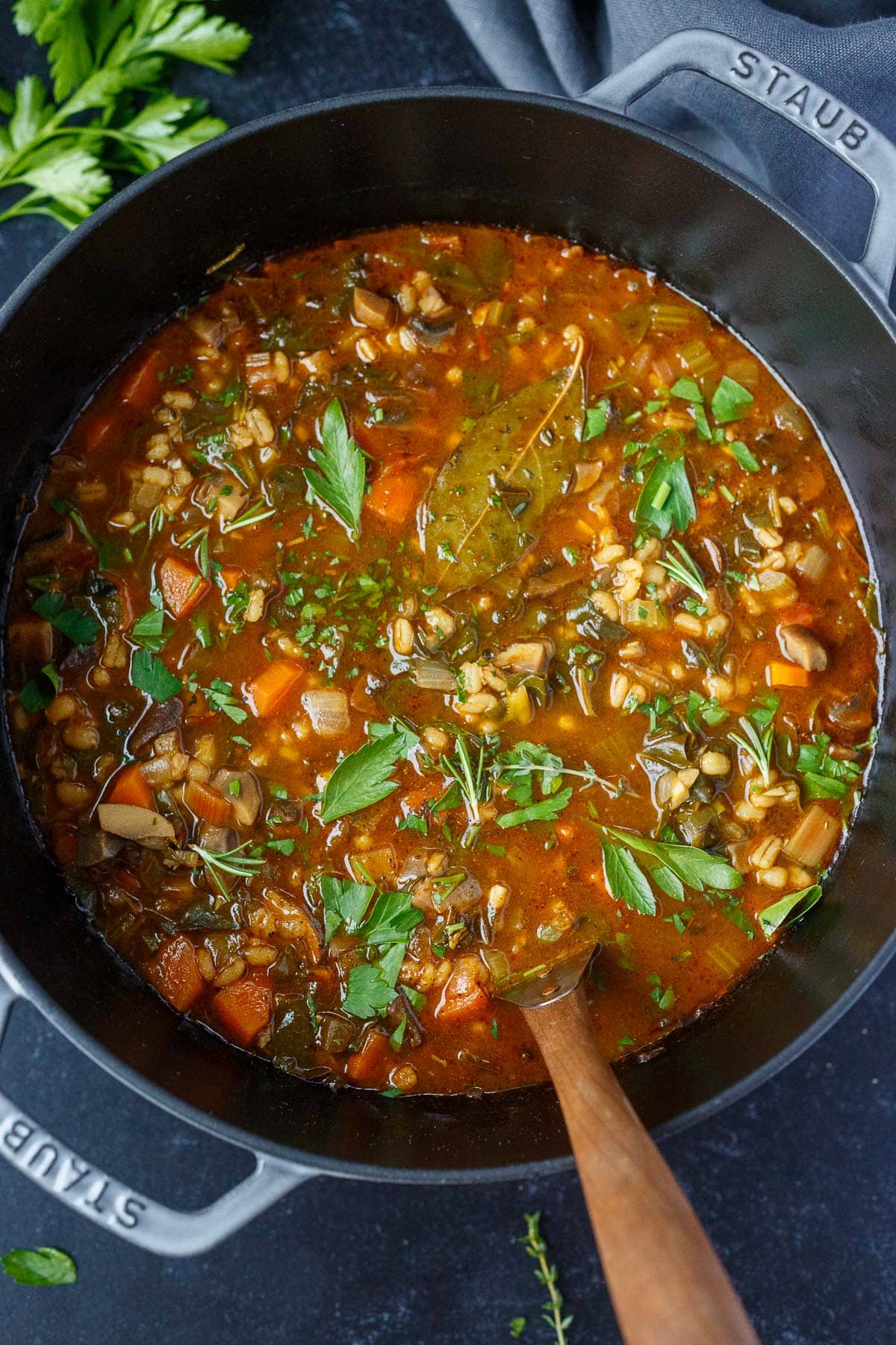 Dutch oven with vegetable barley soup with bay leaf and fresh parsley.