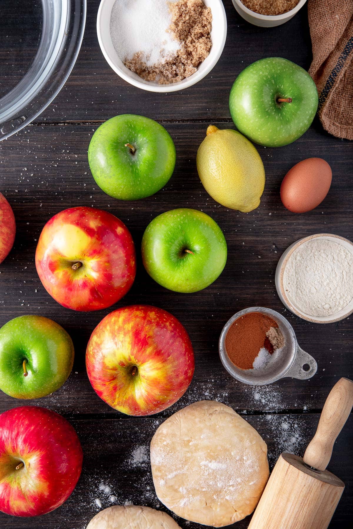 apple pie ingredients - sugar, apples, lemon, egg, flour, spices, pie dough, rolling pin.
