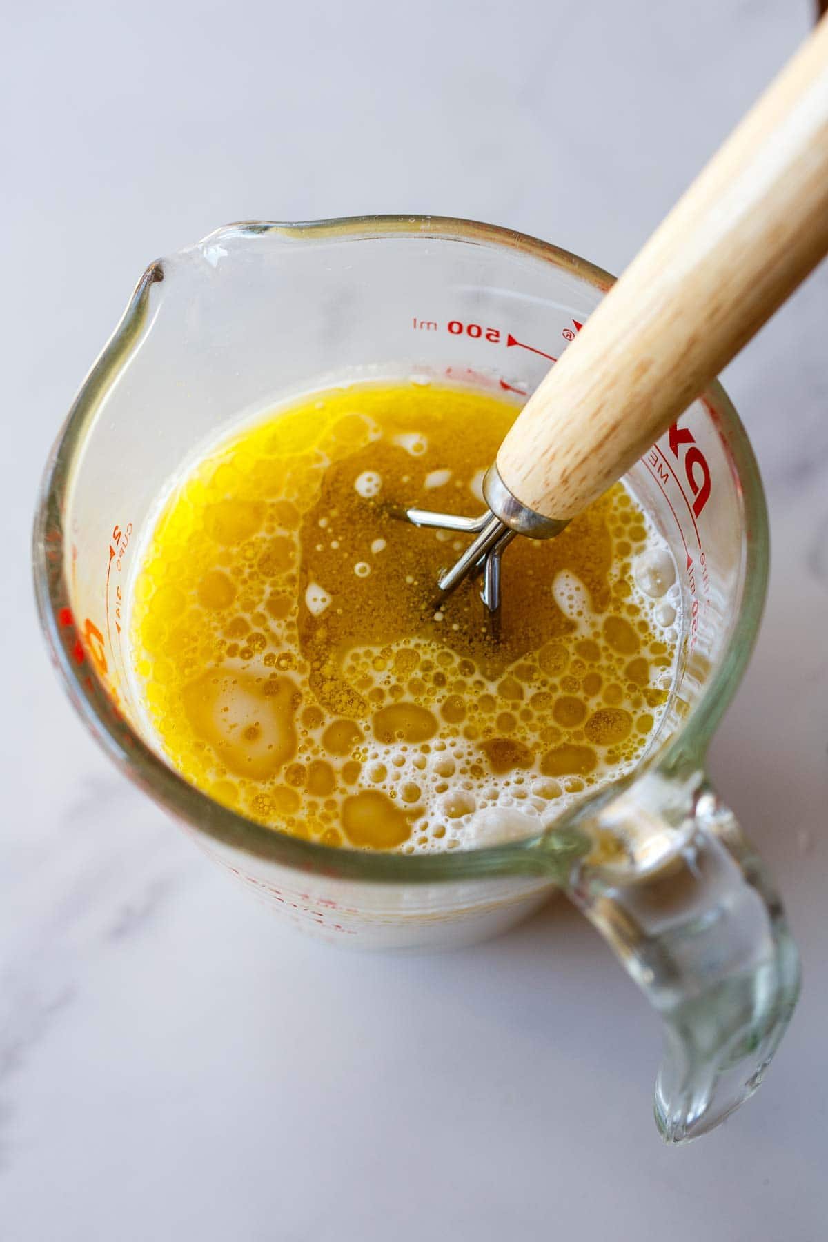 glass measuring cup and whisk with wet ingredients for cranberry orange muffins.