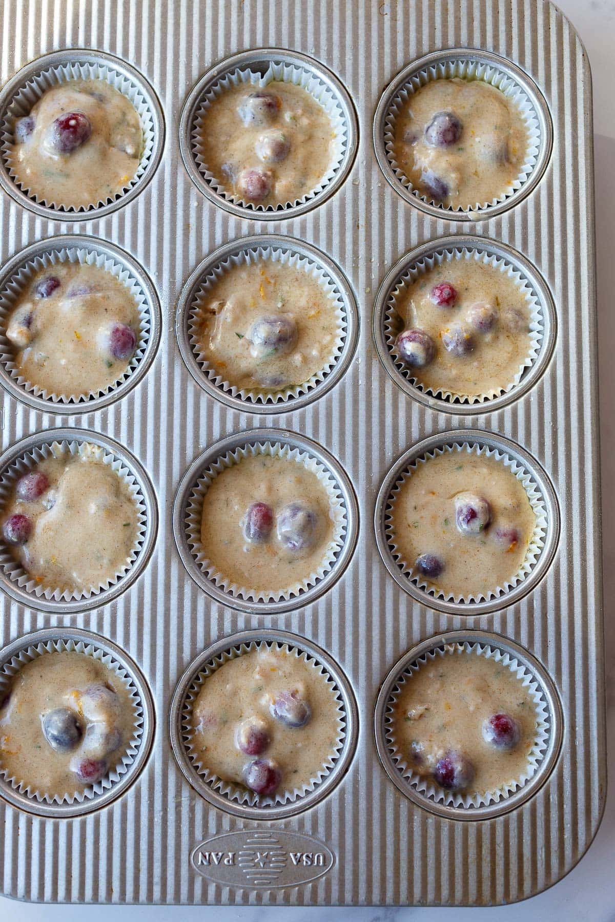 muffin tin with cranberry orange muffin batter divided among paper cups. 