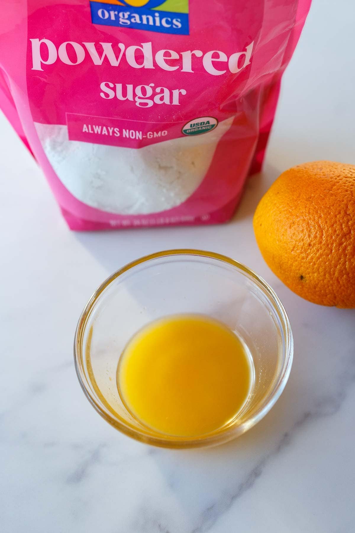 Powdered sugar bag and orange juice in a small bowl.