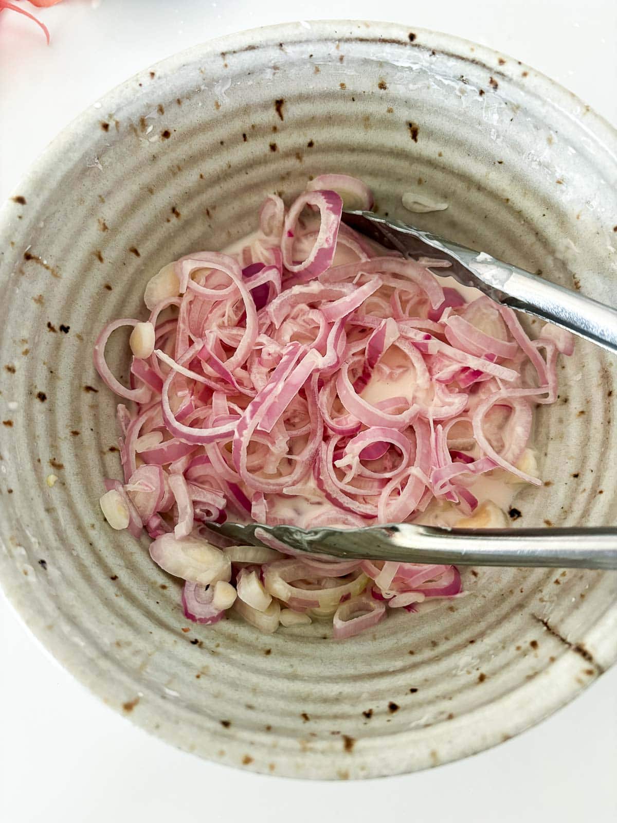 tongs tossing shallot rings in batter.