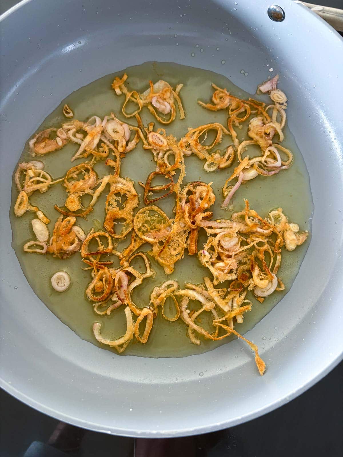 crispy shallots frying in oil in skillet.