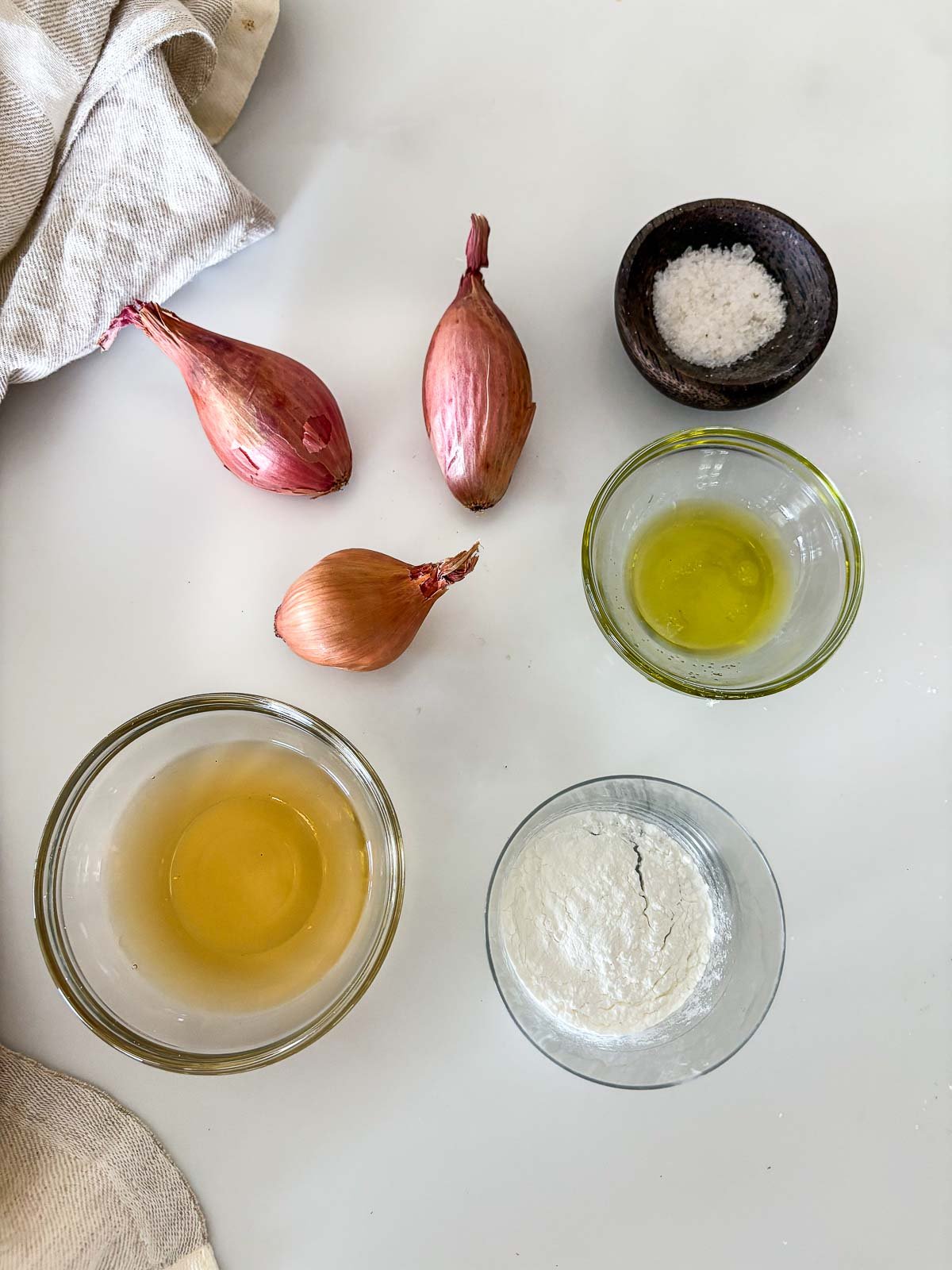 ingredients for crispy shallots - small dishes of salt, vinegar, cornstarch, and oil, next to three shallots. 
