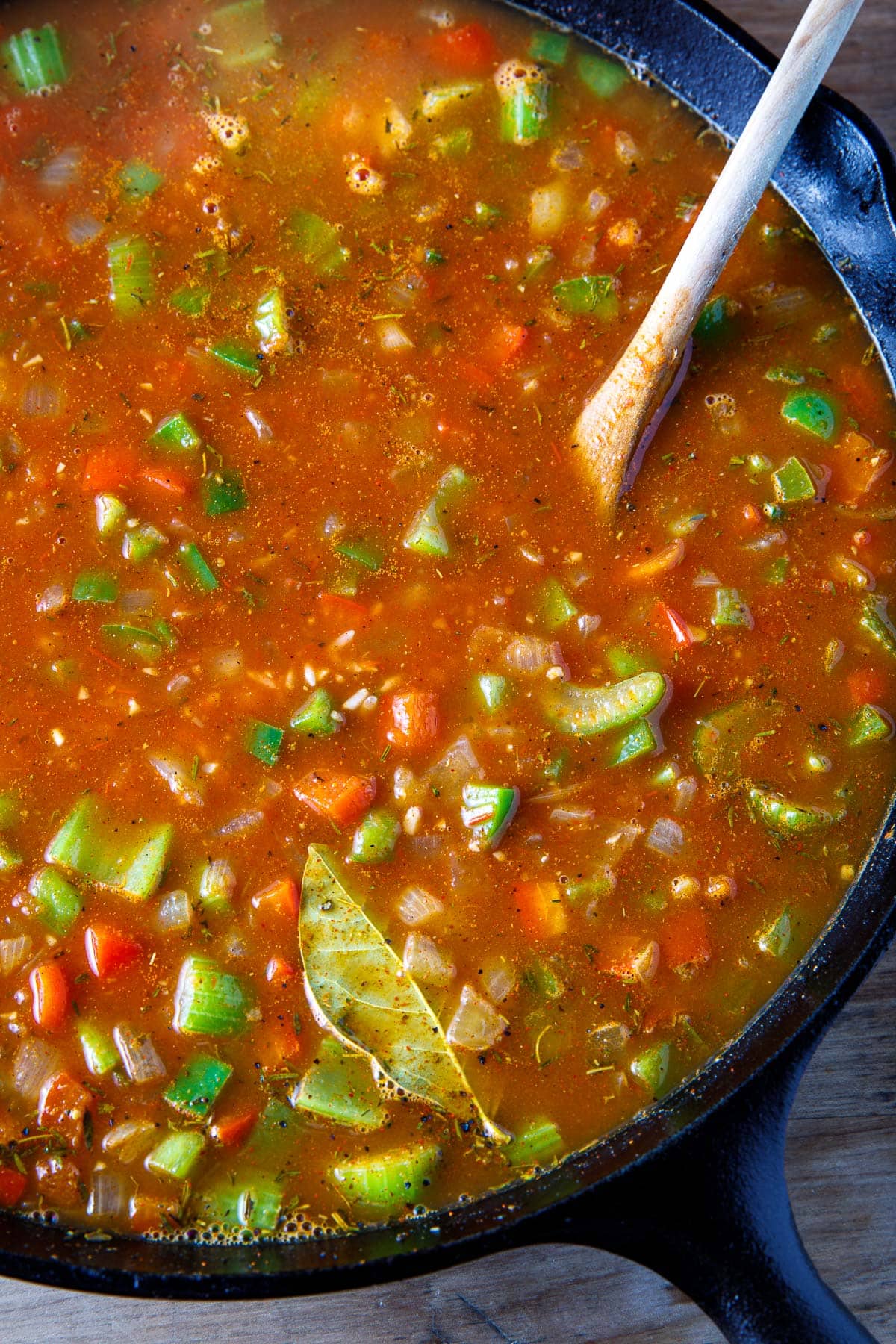 skillet with ingredients for jambalaya simmering - celery, peppers, onion, bay leaves, spices, and broth.