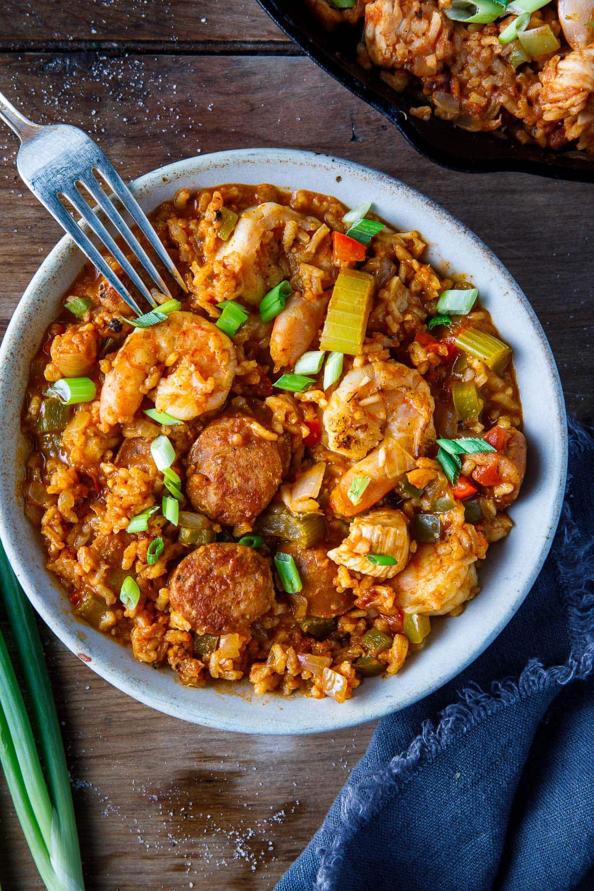bowl of jambalaya with shrimp, chicken sausage, and chicken, with veggies and scallions.
