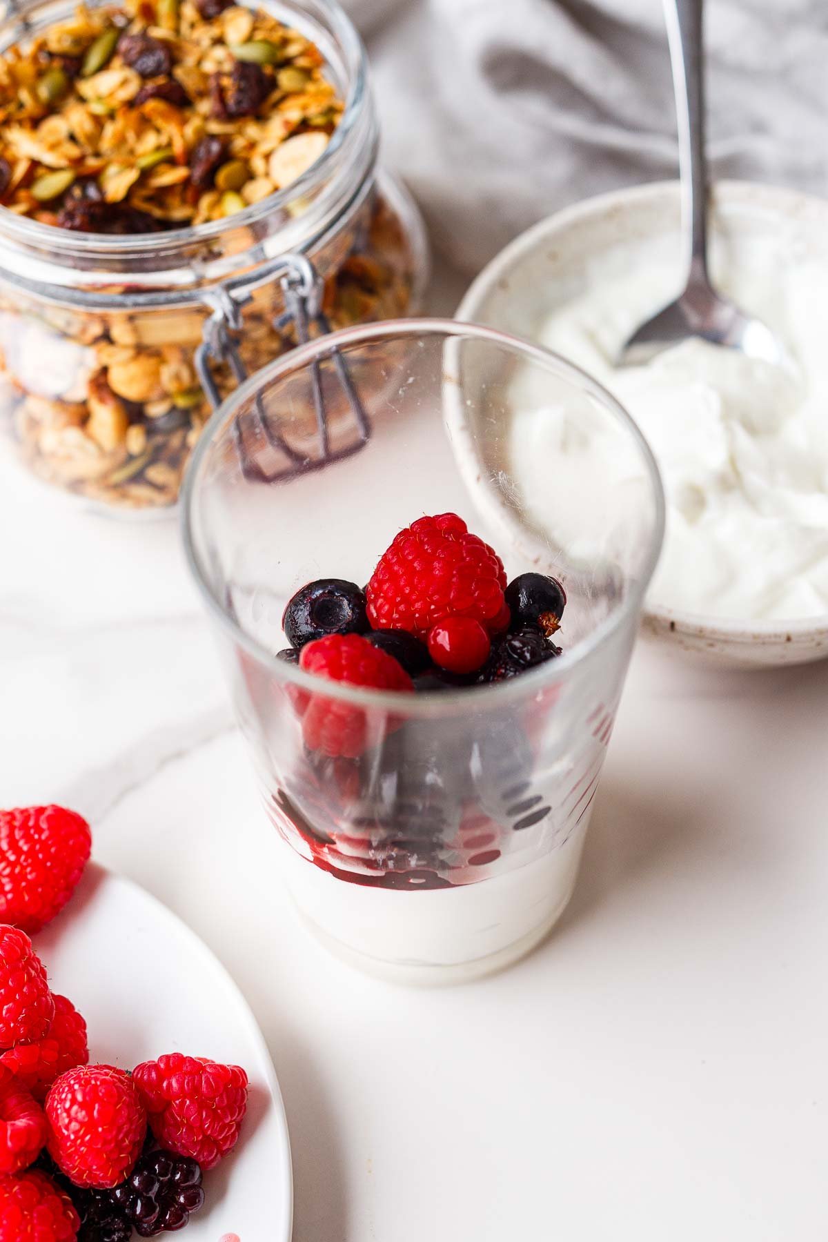 assembling a yogurt parfait - glass jar with yogurt and raspberries and blueberries.