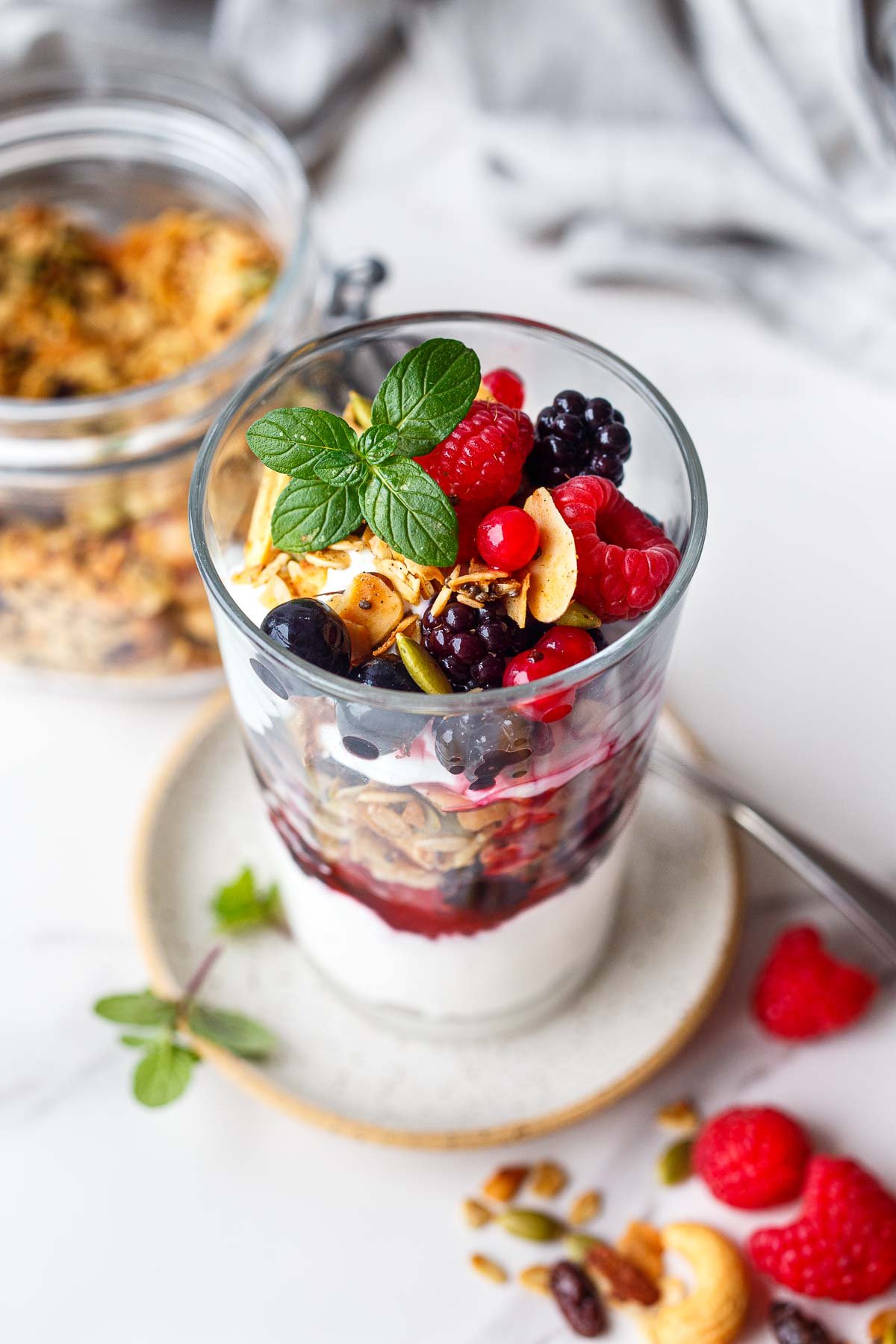 yogurt parfait in glass jar with fresh fruit and granola and fresh herbs.