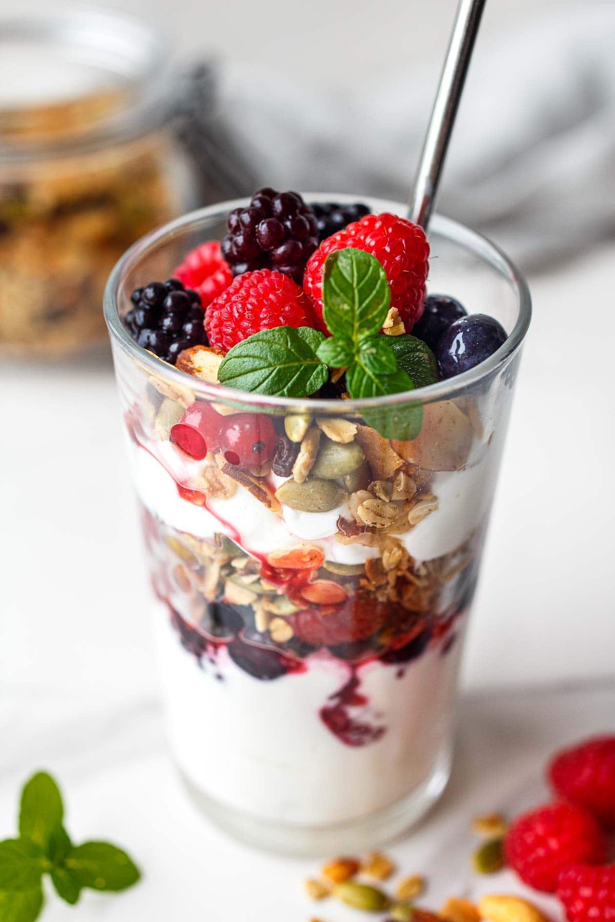 glass jar yogurt parfait with layers of fresh fruit and granola topped with raspberries and blackberries and basil.