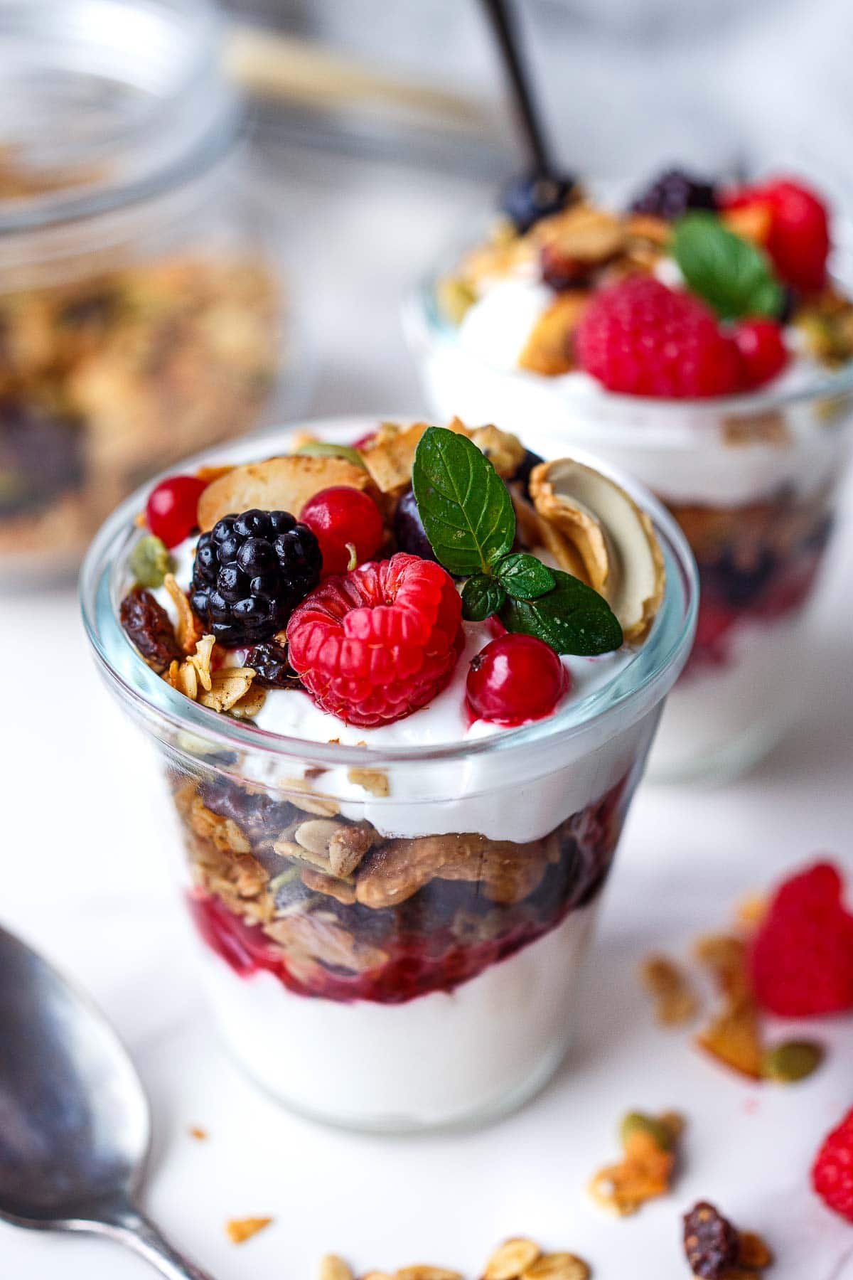 glass jar with yogurt parfait, fruit, and granola, topped with raspberries and blackberries and basil.