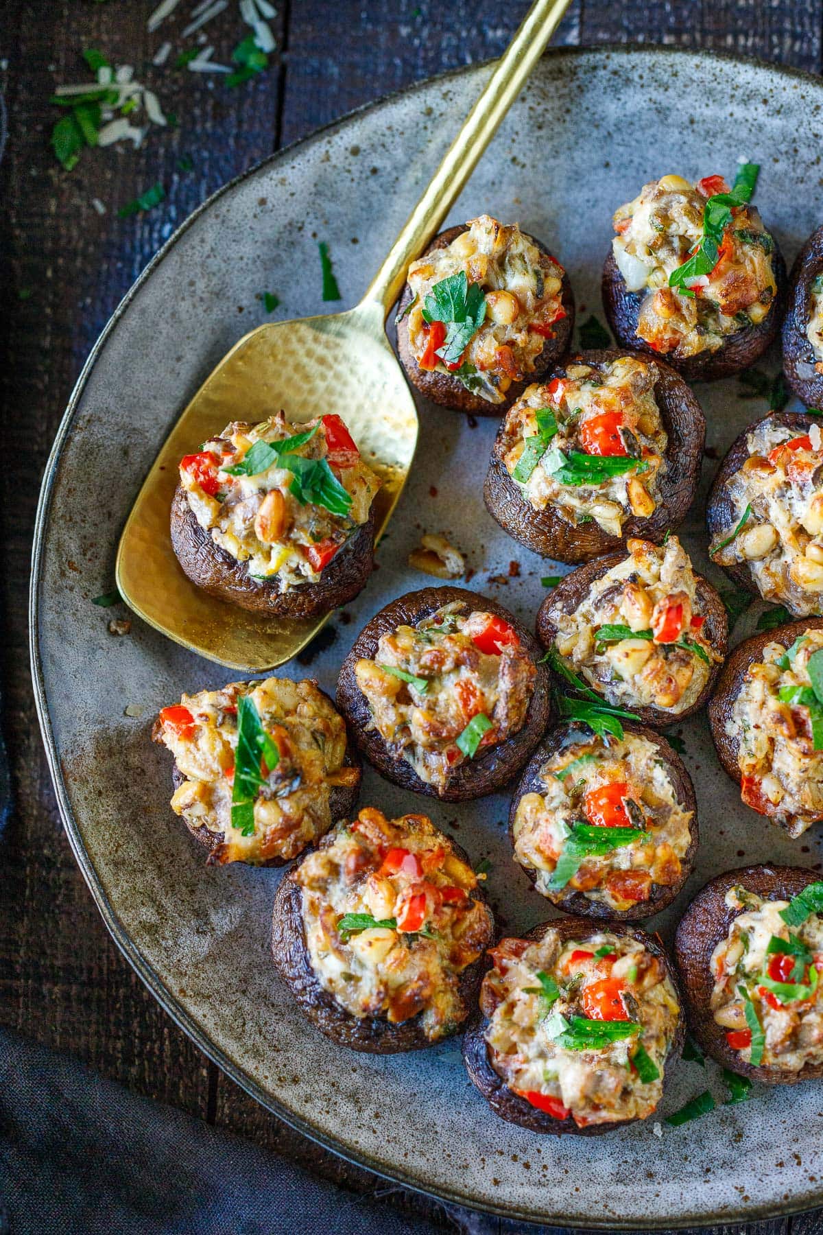 stuffed mushrooms with pinenuts and red peppers on plate with golden tops, garnished with parsley.