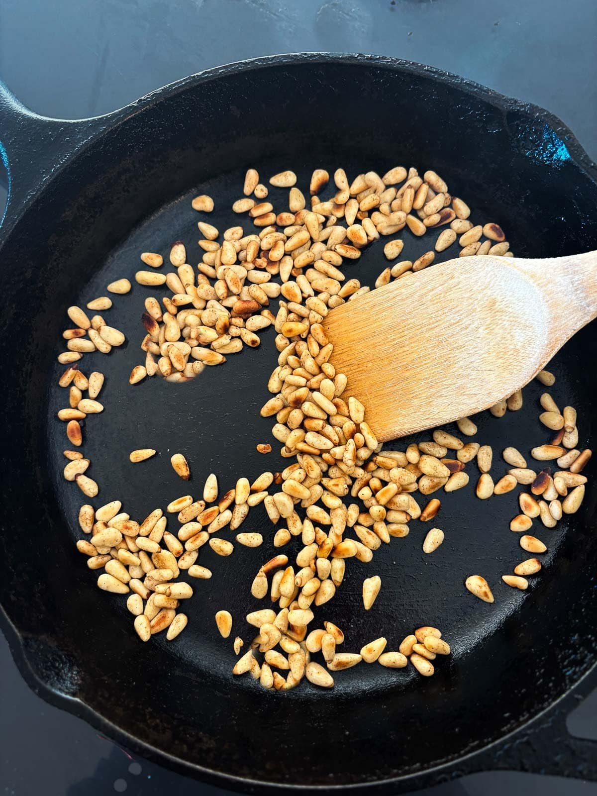 wood spatula stirring toasted pine nuts in cast iron skillet.