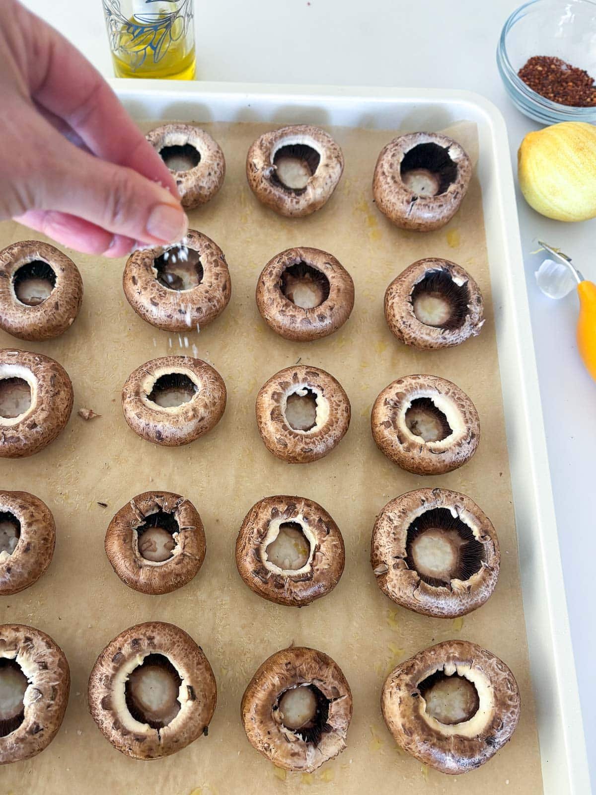 hand sprinkling salt over mushroom caps on parchment-lined baking sheet.