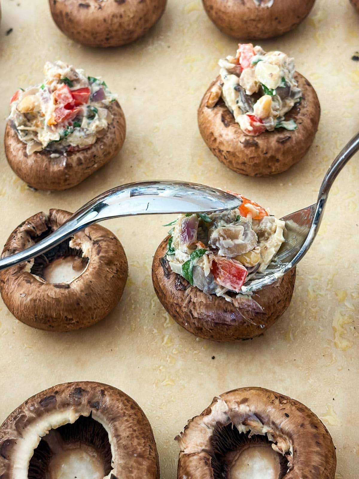 two silver spoons scooping stuffing into a mushroom cap.