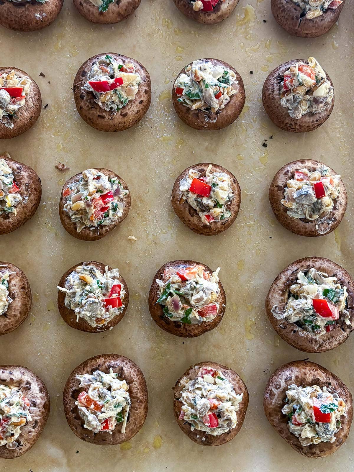 stuffed mushrooms assembled on a parchment lined baking sheet.