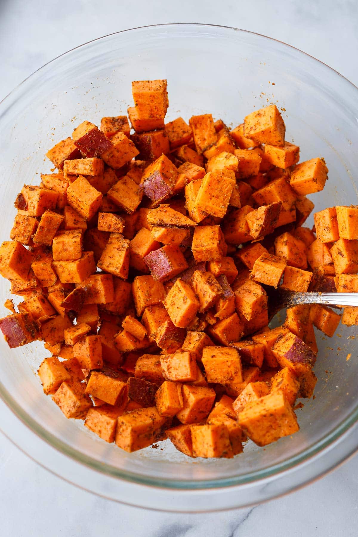 glass bowl with cubed sweet potato tossed in seasoning.