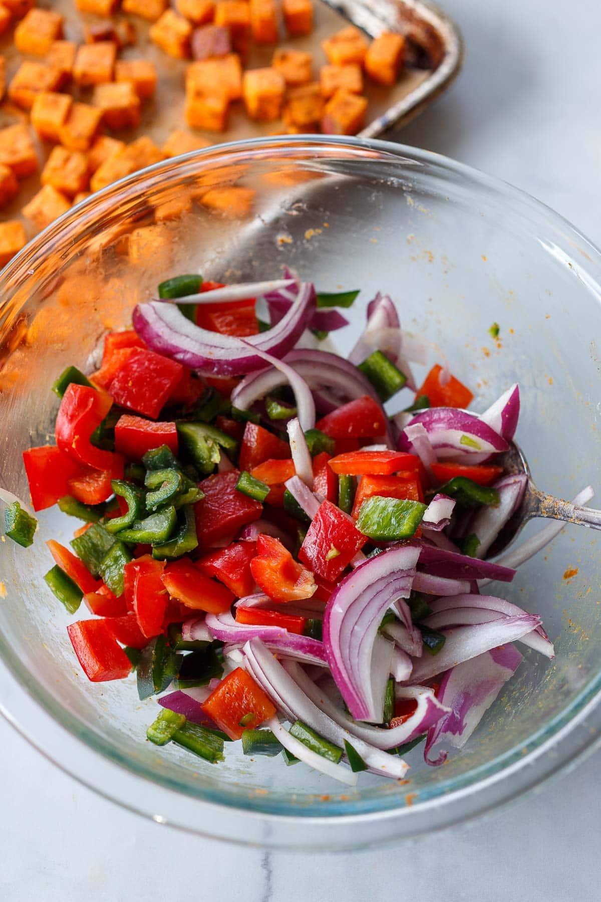 glass bowl with red bell pepper, poblano, and red onion, tossed in seasoning.